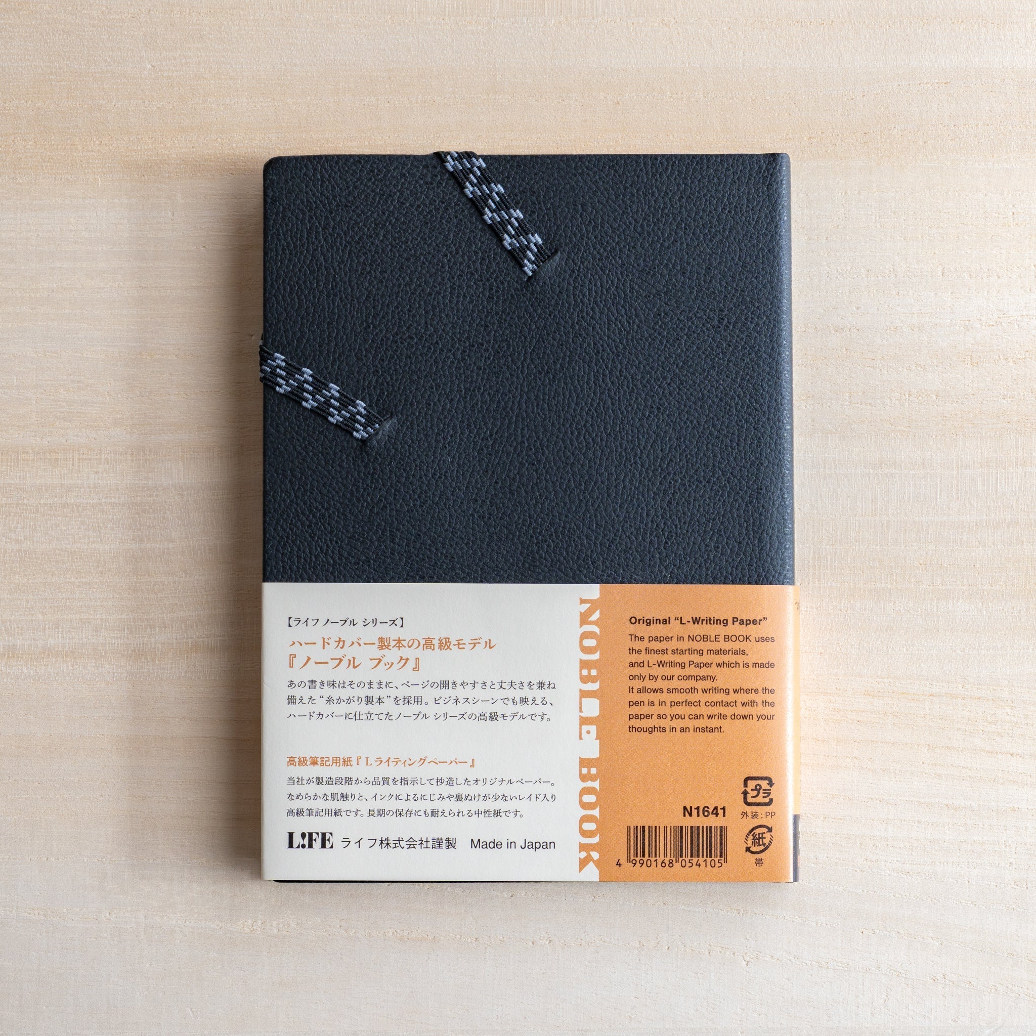 Life Noble notebook A6 hard cover with product band on desk, showing textured black cover and elastic band.
