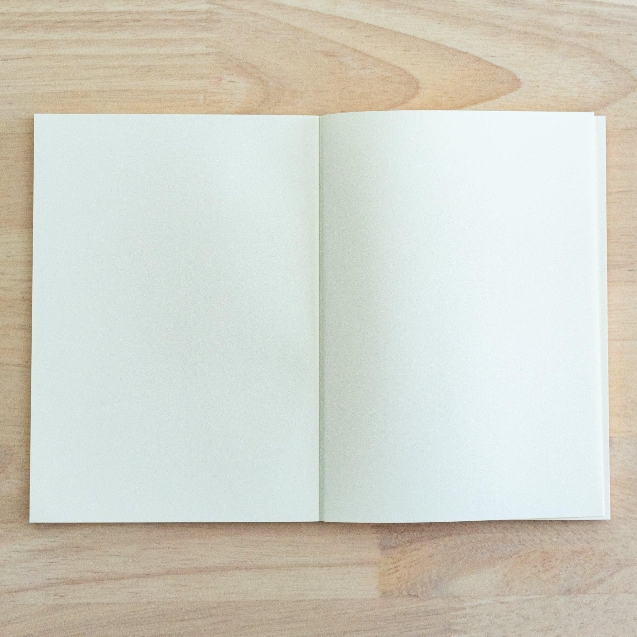 An open A4-size LIFE Noble Note notebook with cream-colored, lined pages and a smooth texture, placed on a wooden surface.