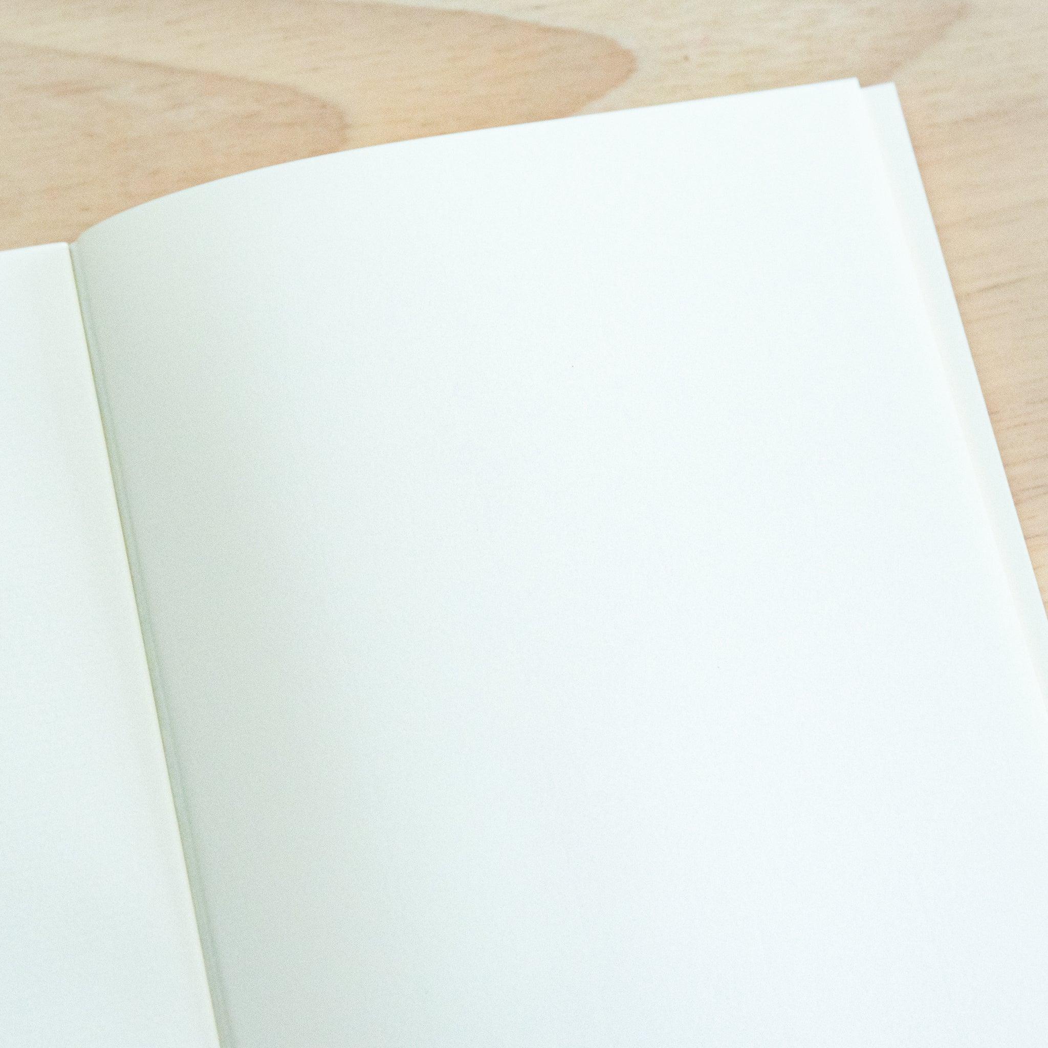 An open A4-size LIFE Noble Note notebook with cream-colored, lined pages and a smooth texture, placed on a wooden surface.