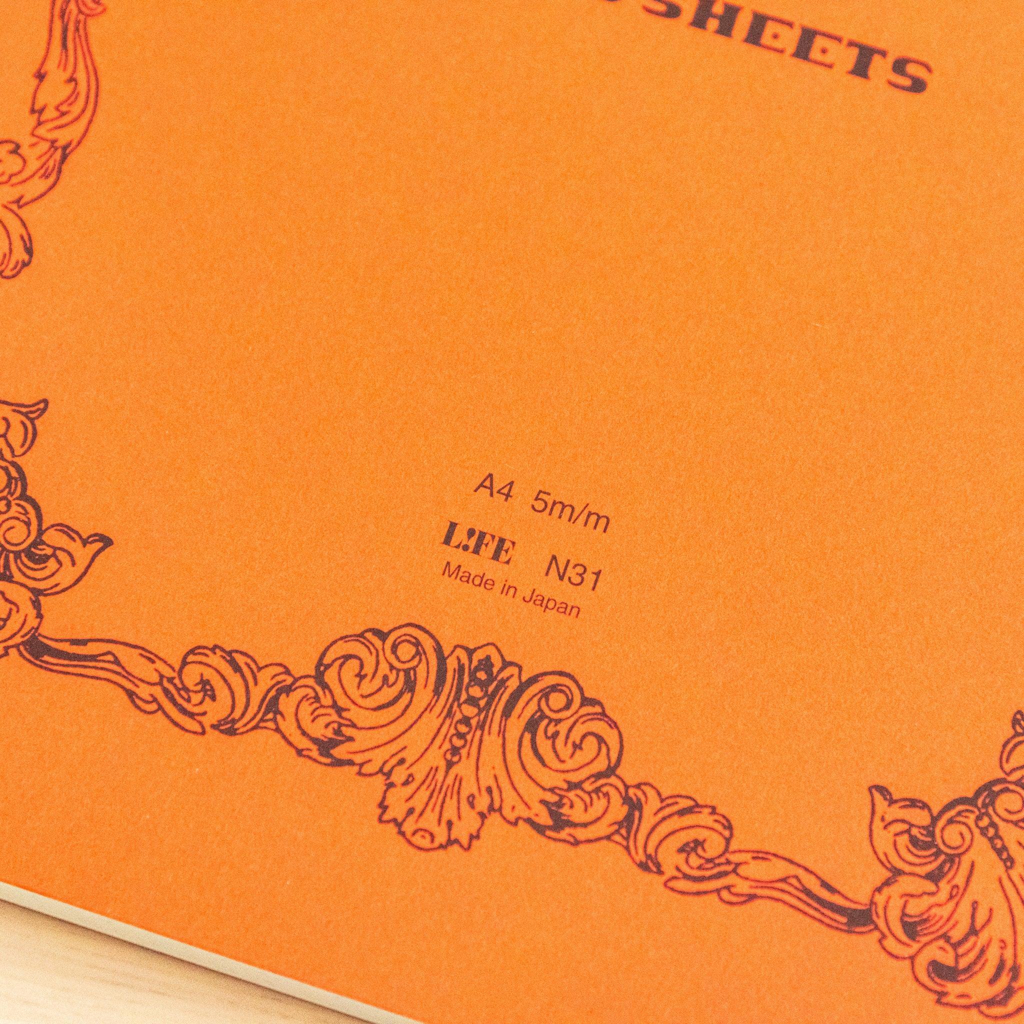 A single "LIFE Noble Note Section" notebook with an orange cover, black spine, ornate border design, and 100 sheets, displayed on a wooden surface.