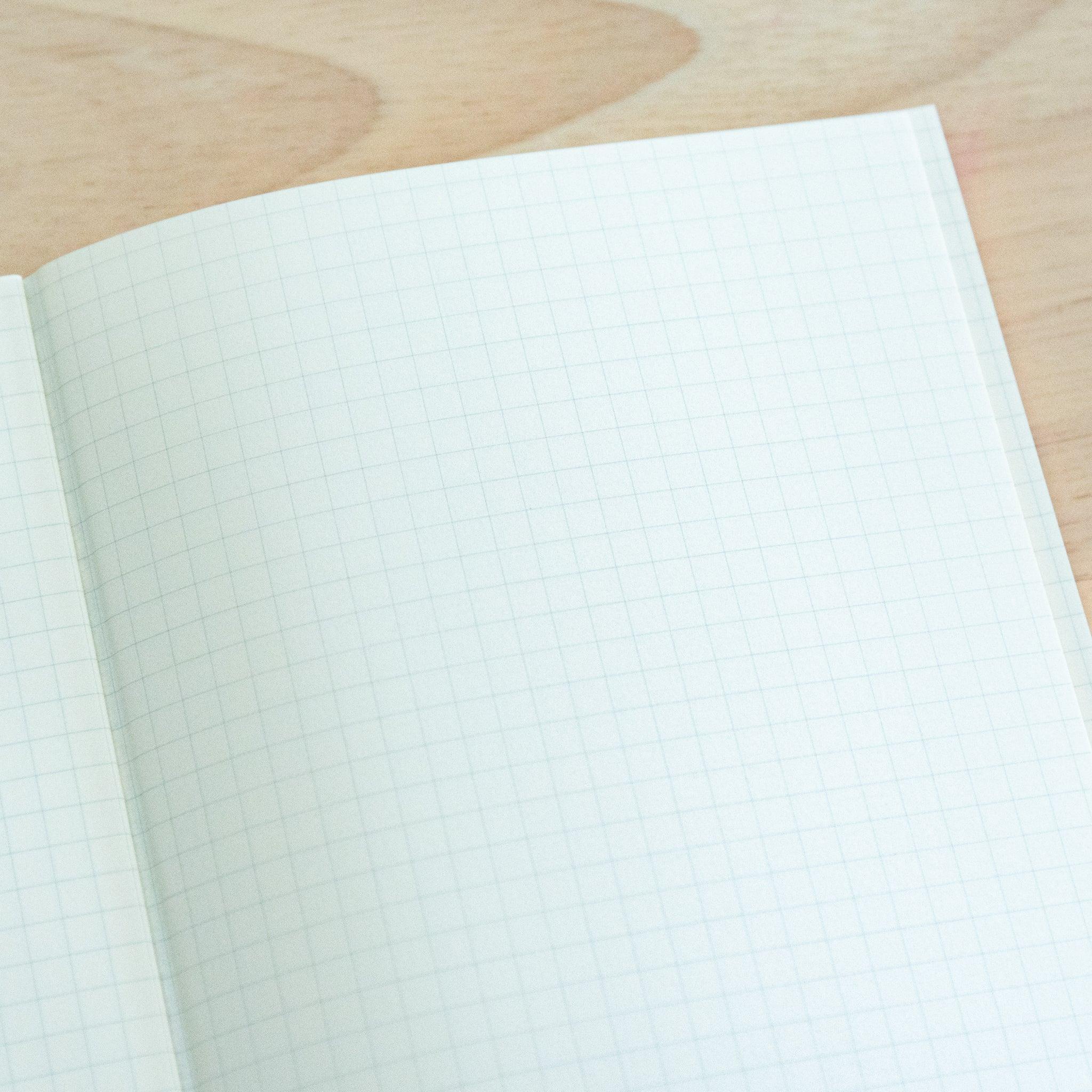 An open A4-size LIFE Noble Note notebook with cream-colored, lined pages and a smooth texture, placed on a wooden surface.