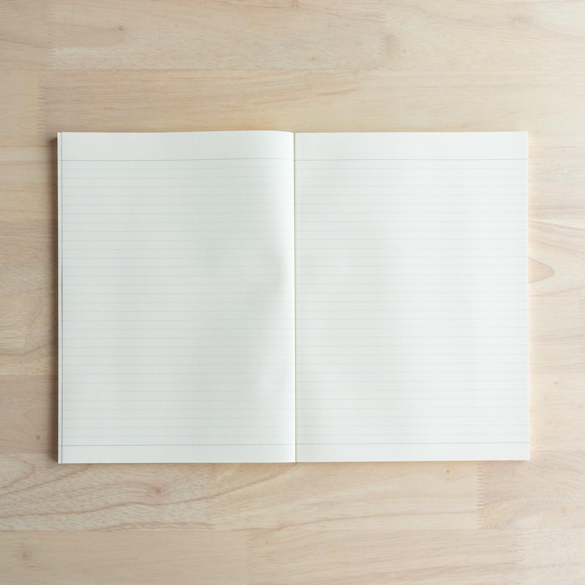 An open A4-size LIFE Noble Note notebook with cream-colored, lined pages and a smooth texture, placed on a wooden surface.