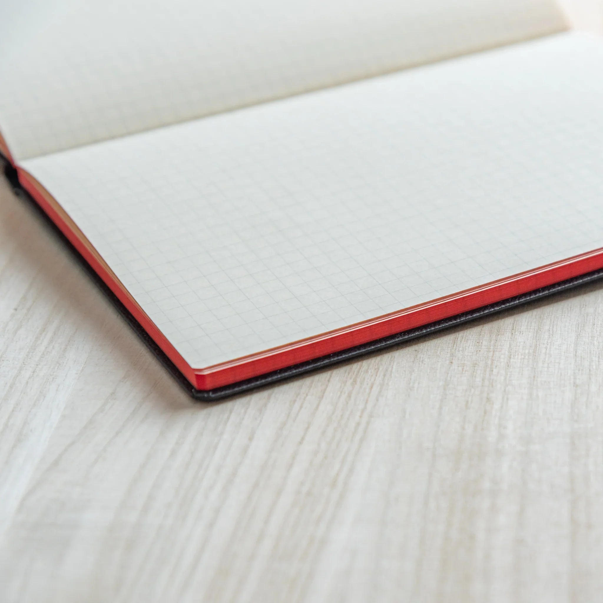 Open Drescco Japanese journal showing light grid pages with red page edges and dark cover resting on wooden desk.