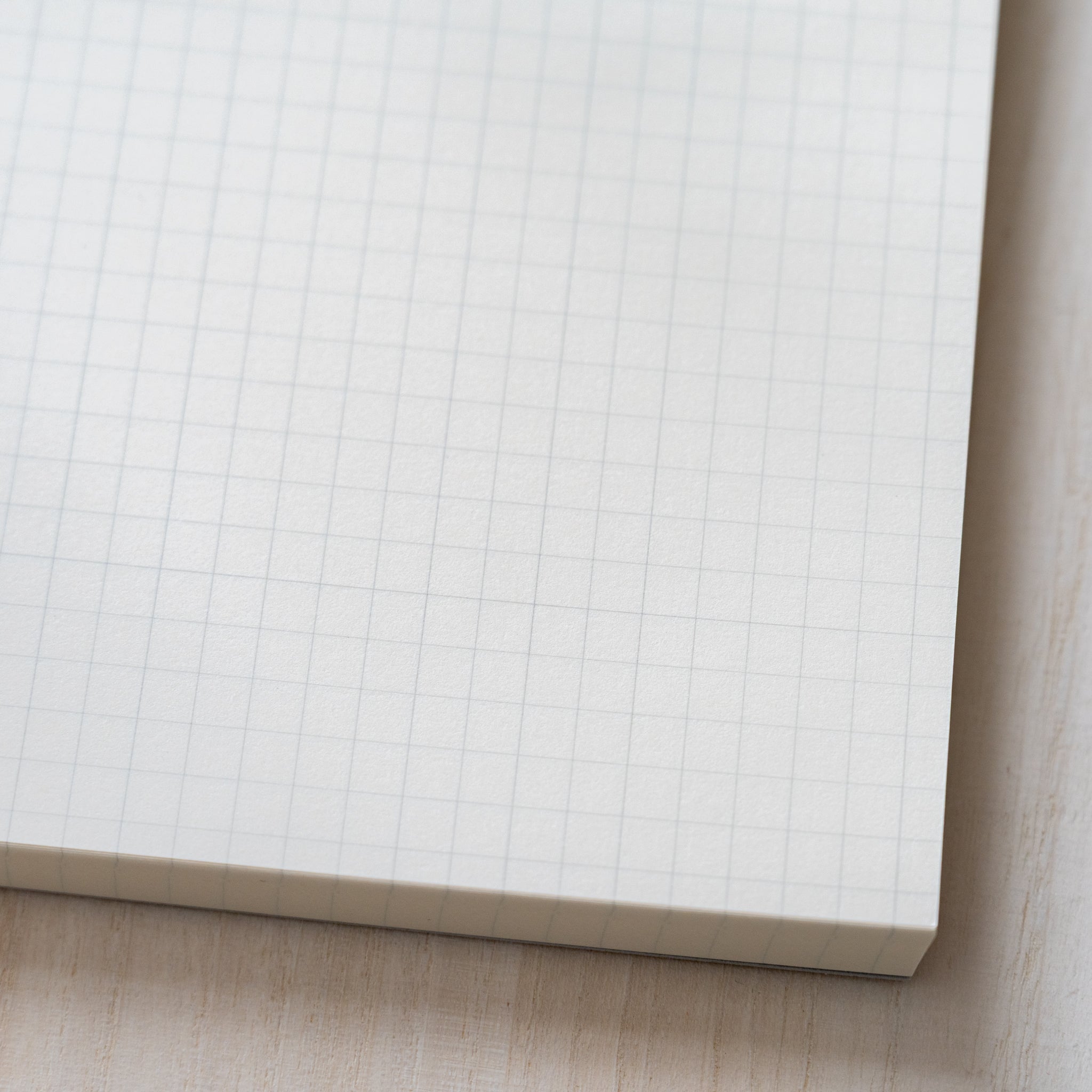 Life noble writing pad B6 close-up of grid page corner, cream L Writing Paper thickness and clean edges on wood desk