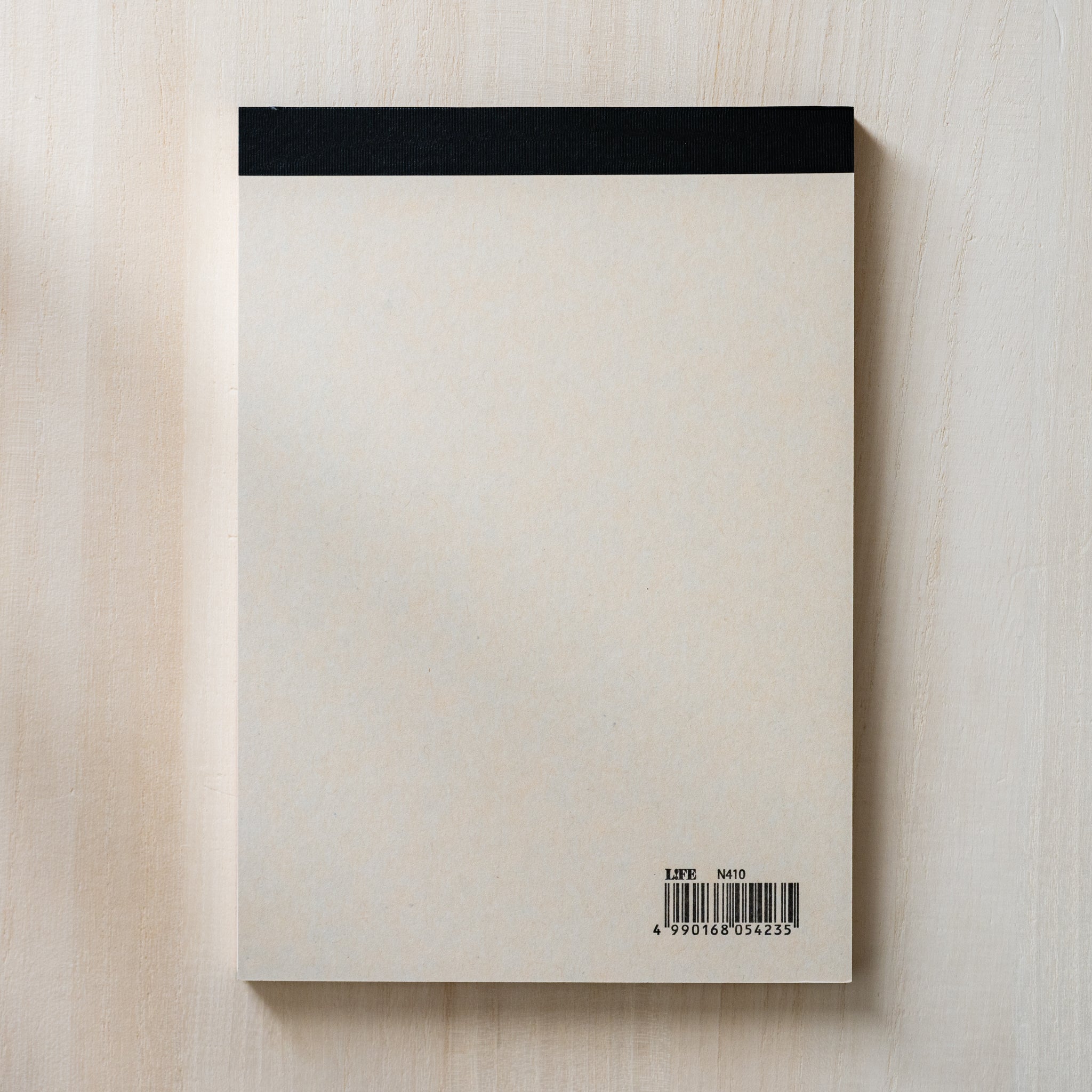 Life noble writing pad B6 back view shown from above, plain cream backing with black top binding and barcode label
