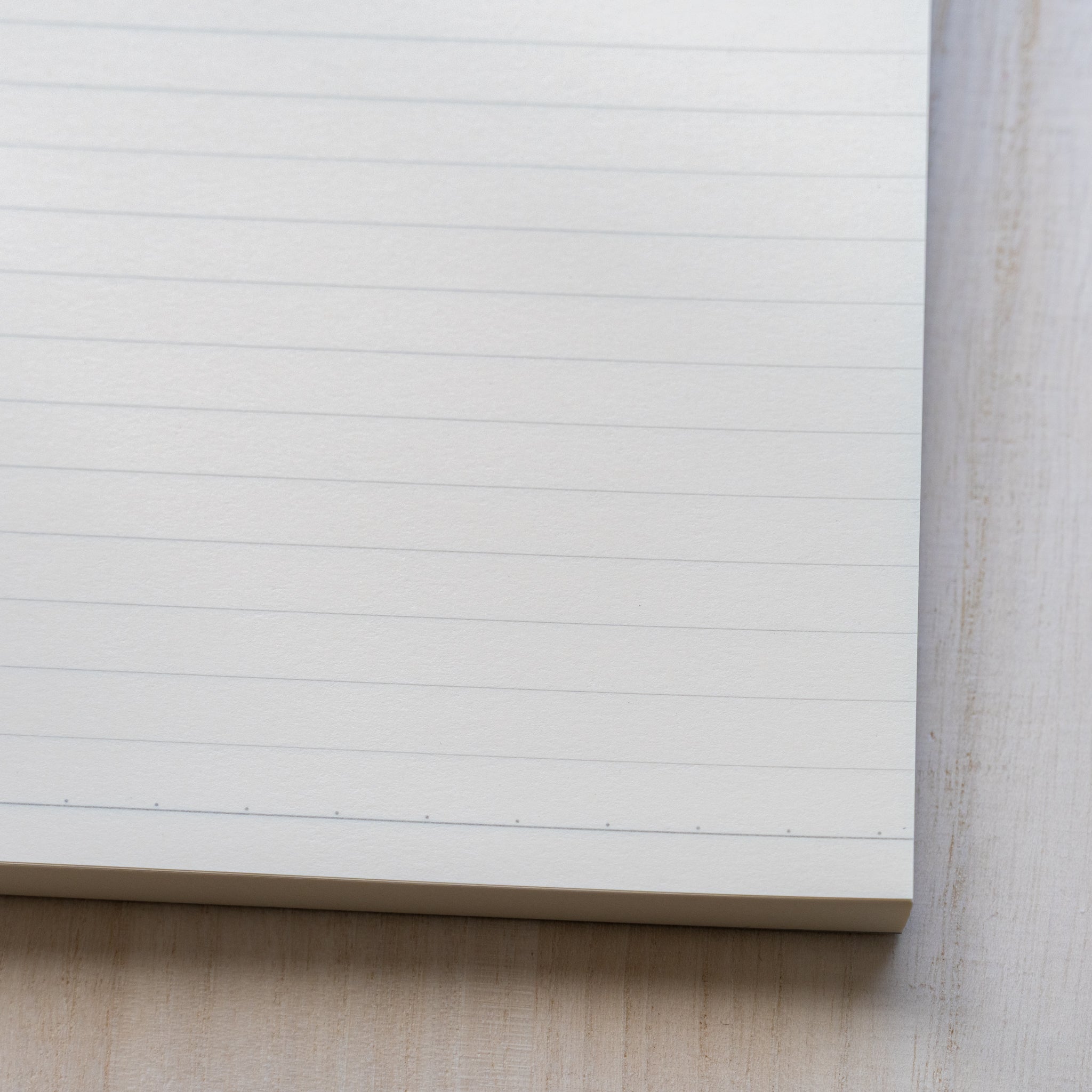 Life noble writing pad B6 close-up of ruled L Writing Paper corner, fine horizontal lines, clean cut edges on light desk