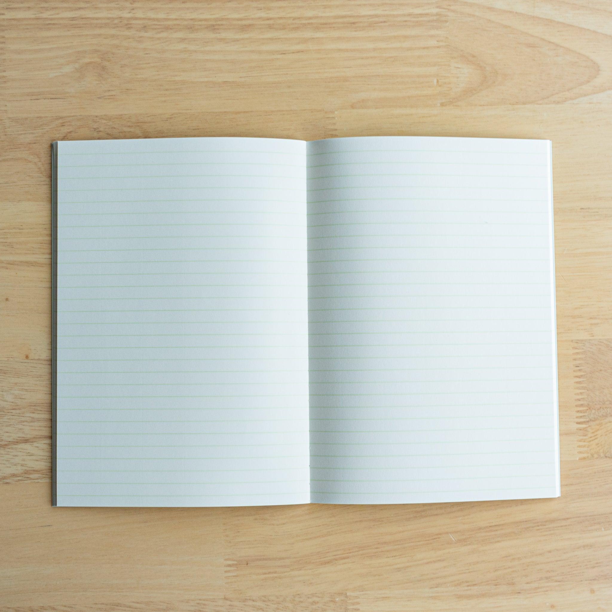 An open Japanese notebook with light green grid paper featuring fine squares, displayed on a wooden surface.