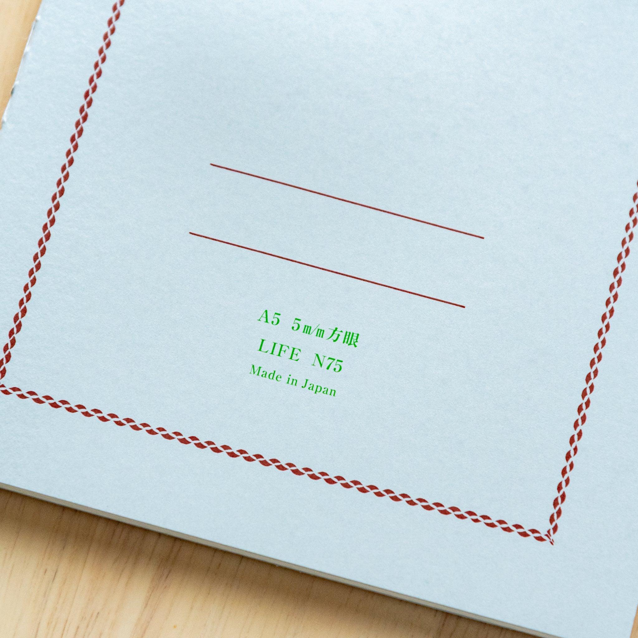 A single "LIFE Pistachio" notebook in A5 size with a light gray cover, green logo, and minimal border design, displayed on a wooden surface.