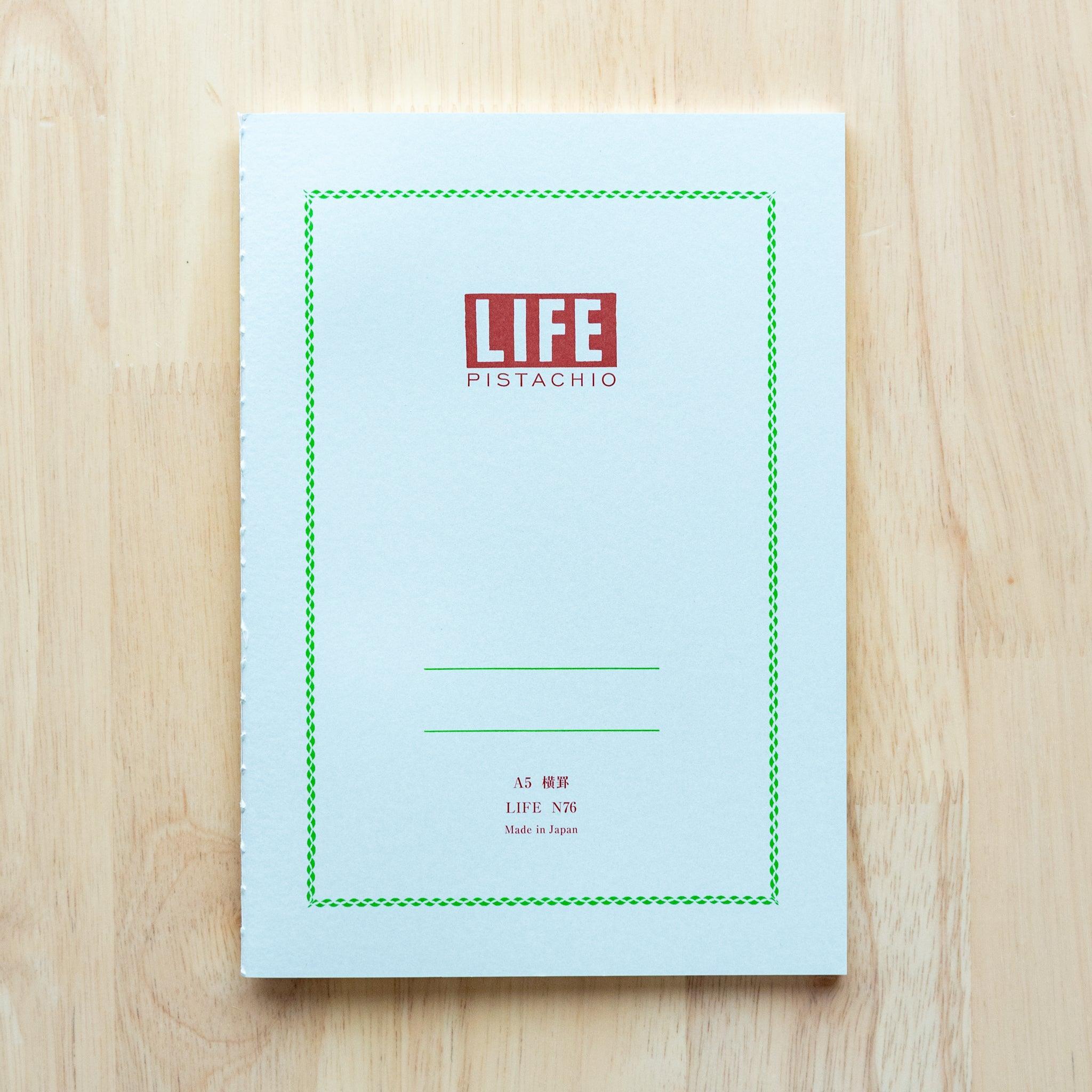 A single "LIFE Pistachio" notebook in A5 size with a light gray cover, red logo, and minimal border design, displayed on a wooden surface.