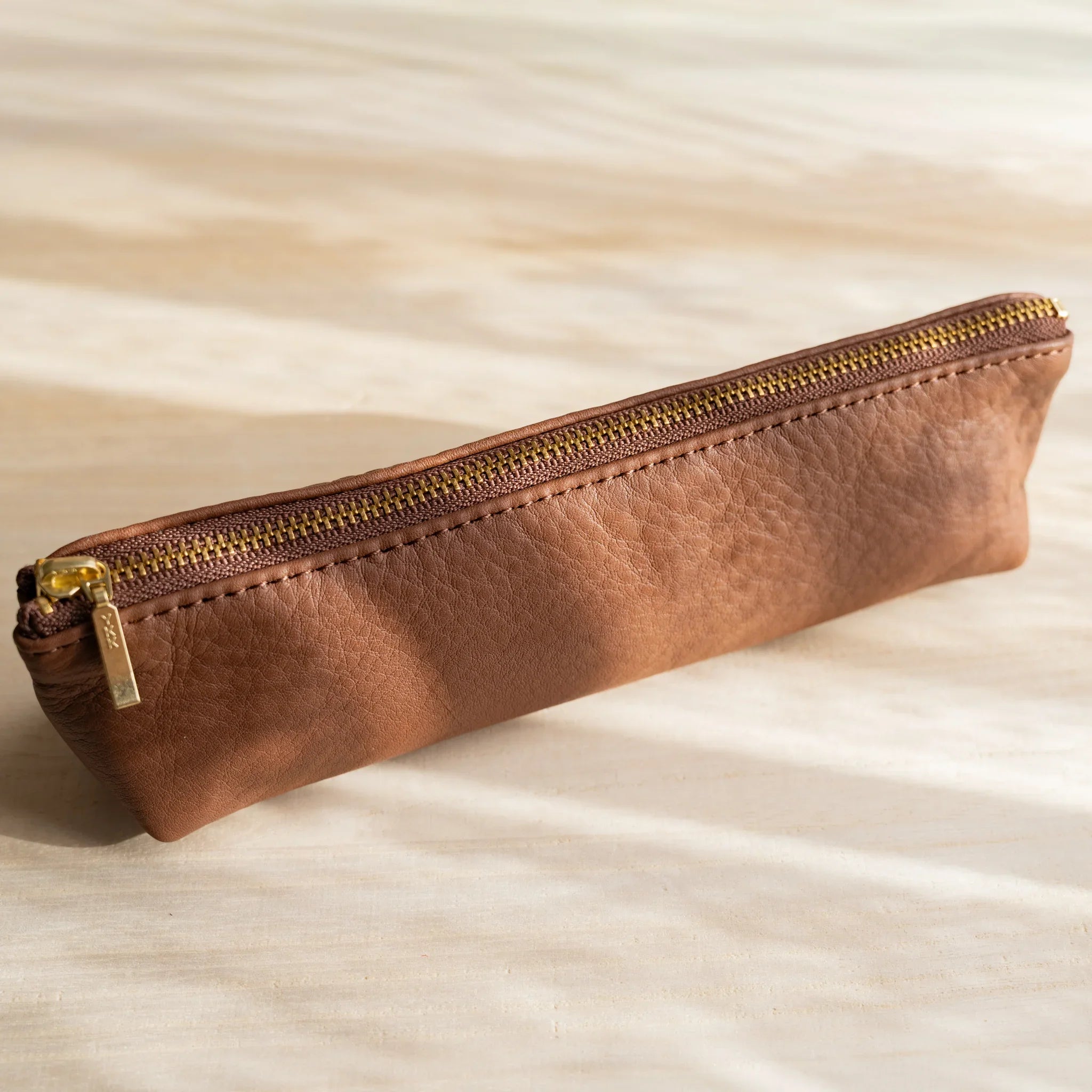 Life steerhide leather pen case in brown with gold zipper and cylindrical form and features and features
