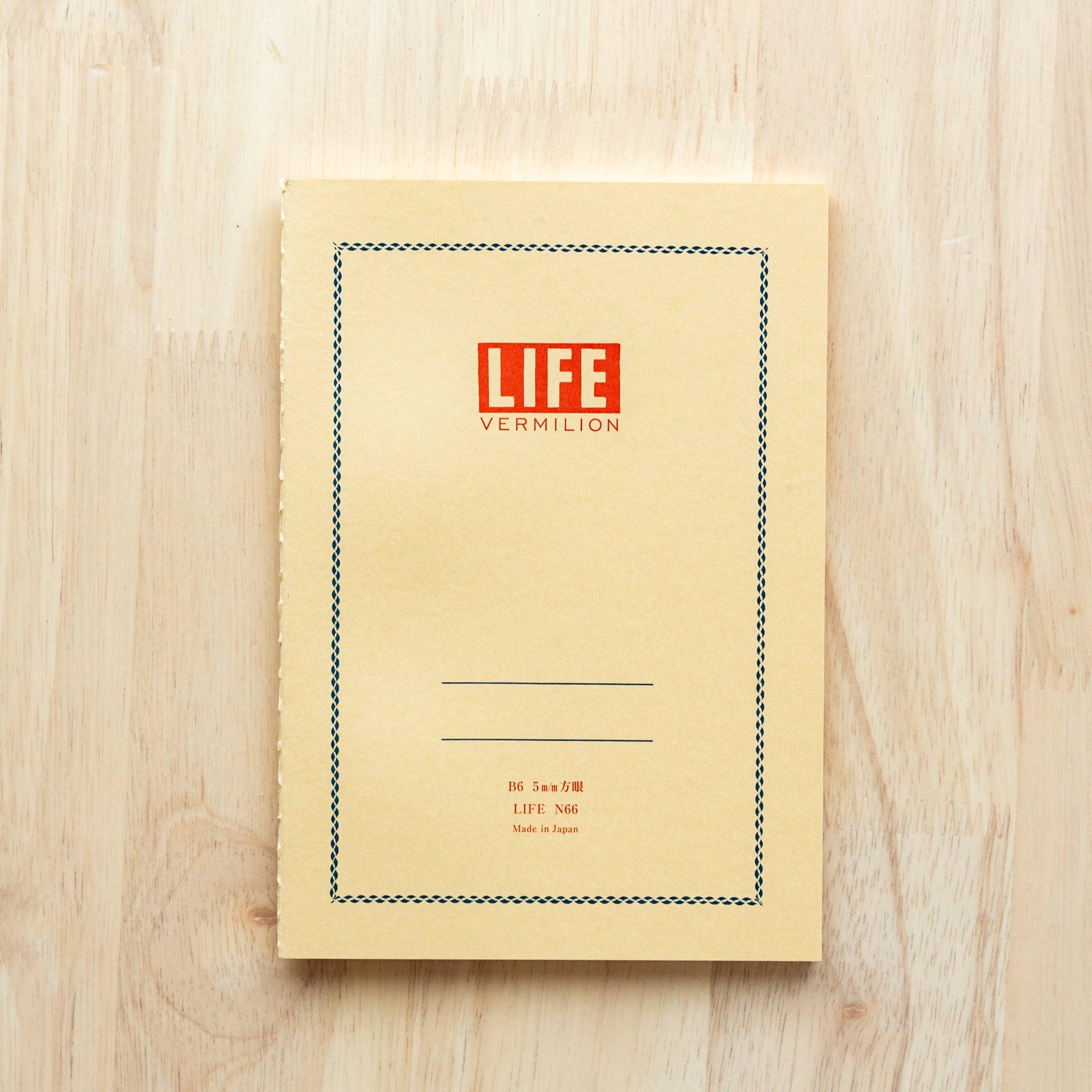 A single "LIFE Vermilion" notebook in A5 size with a beige cover, red logo, and minimal border design, displayed on a wooden surface.