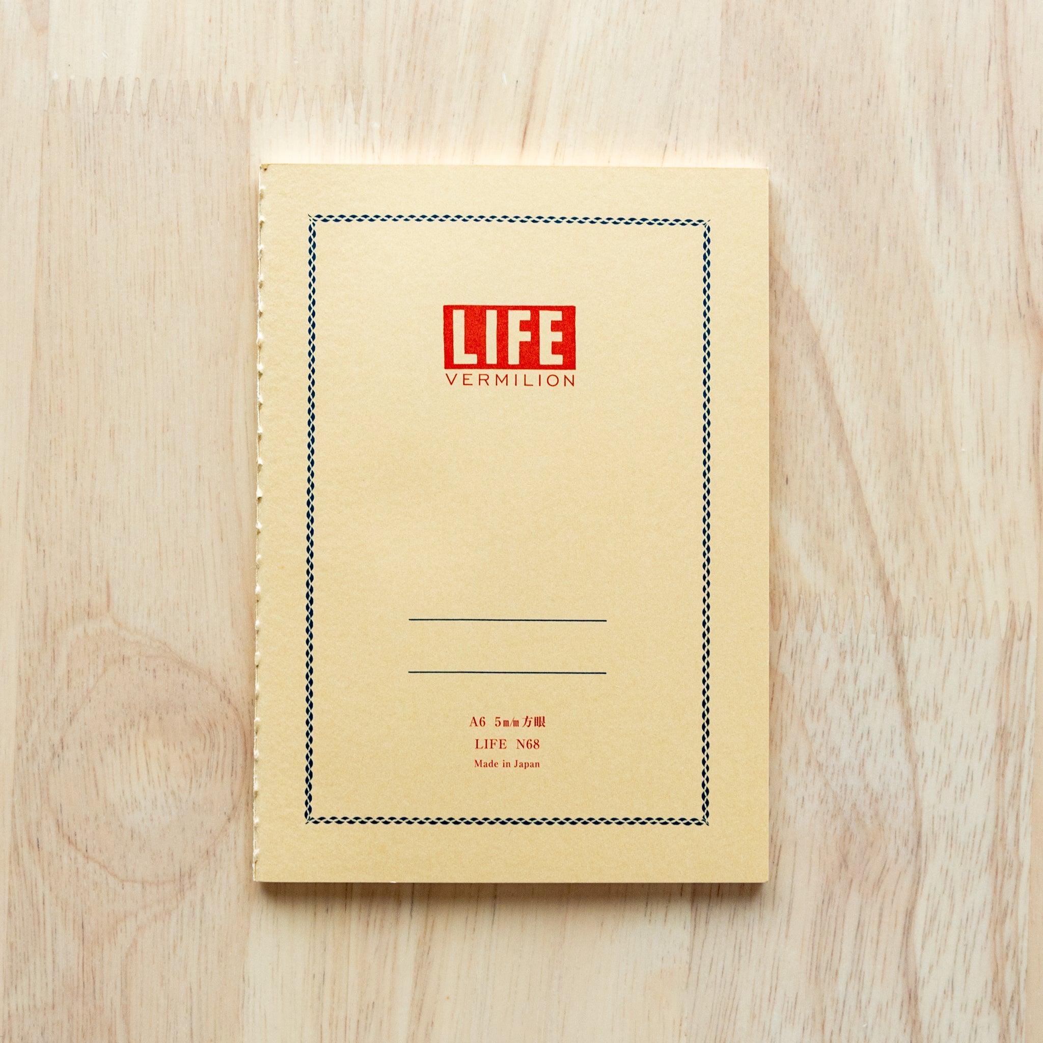 A single "LIFE Vermilion" notebook in A5 size with a beige cover, red logo, and minimal border design, displayed on a wooden surface.