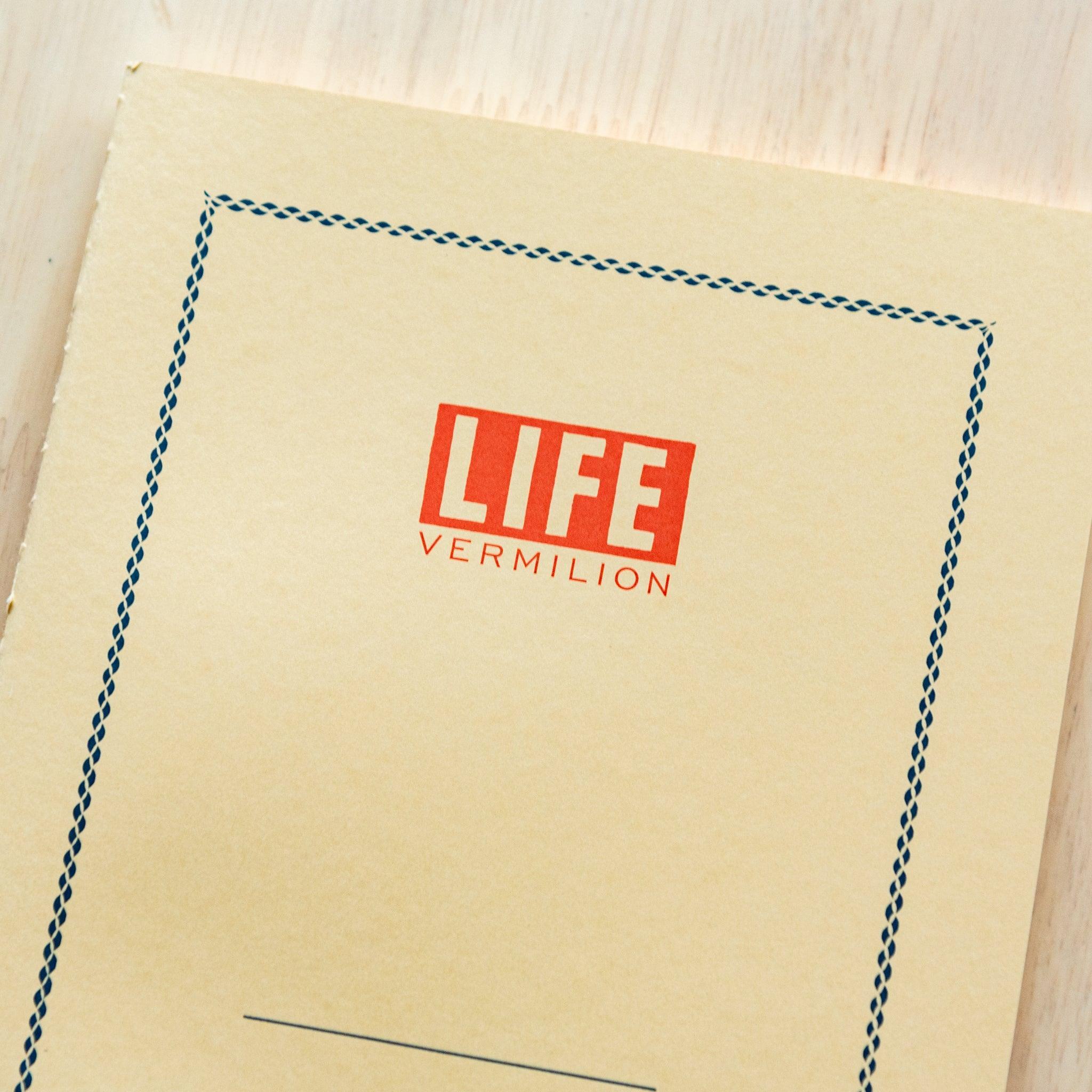 A single "LIFE Vermilion" notebook in A5 size with a beige cover, red logo, and minimal border design, displayed on a wooden surface.