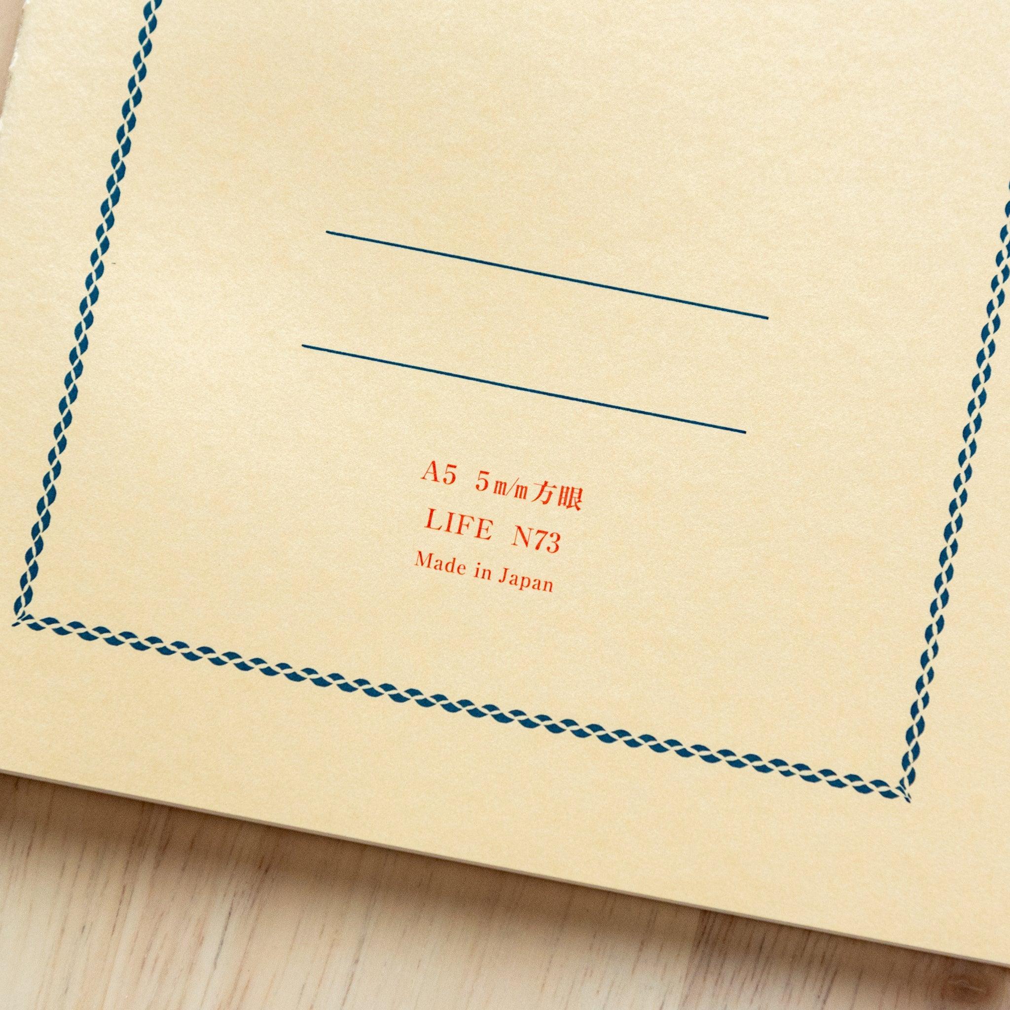 A single "LIFE Vermilion" notebook in A5 size with a beige cover, red logo, and minimal border design, displayed on a wooden surface.