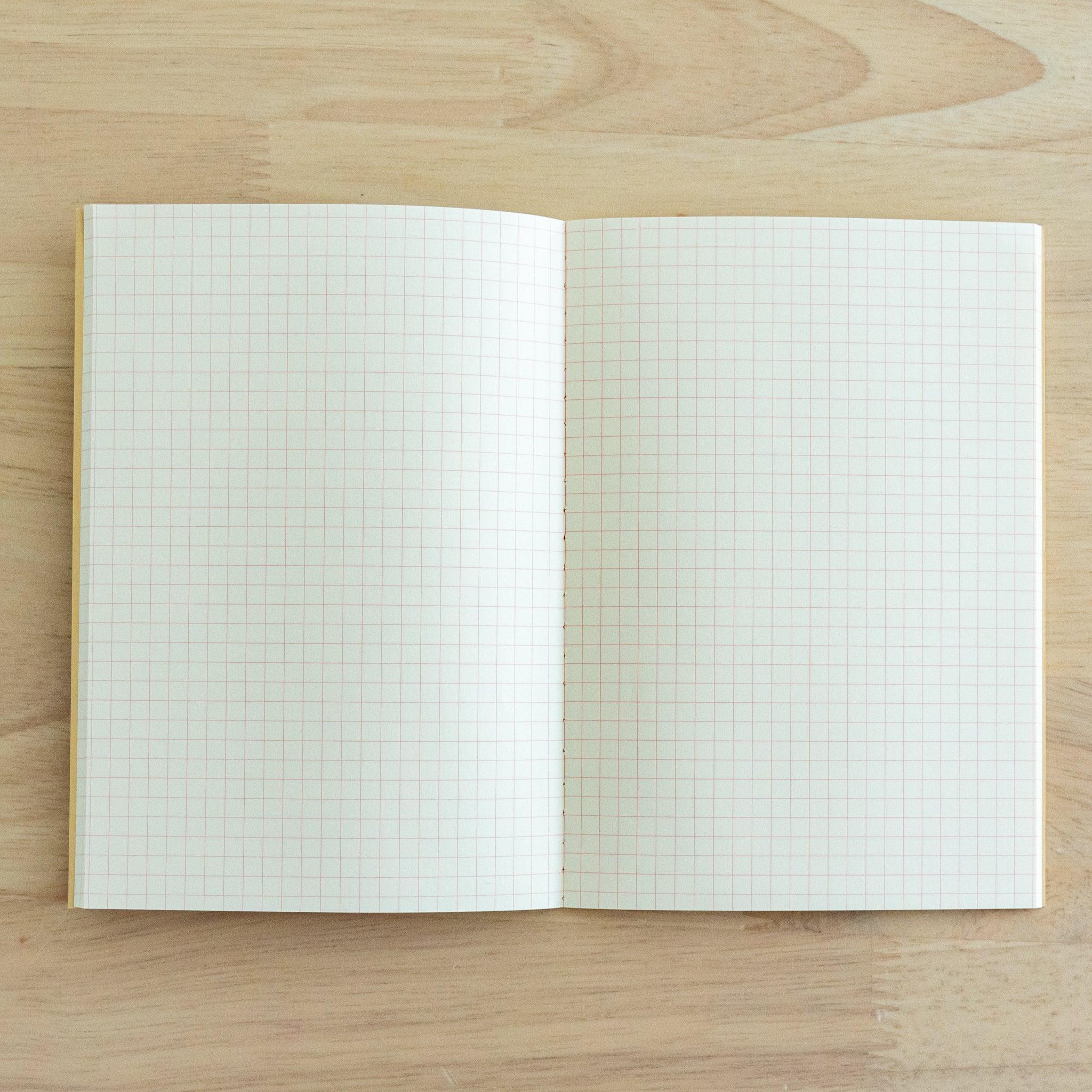 An open notebook with cream-colored grid paper featuring fine red squares, displayed on a wooden surface.