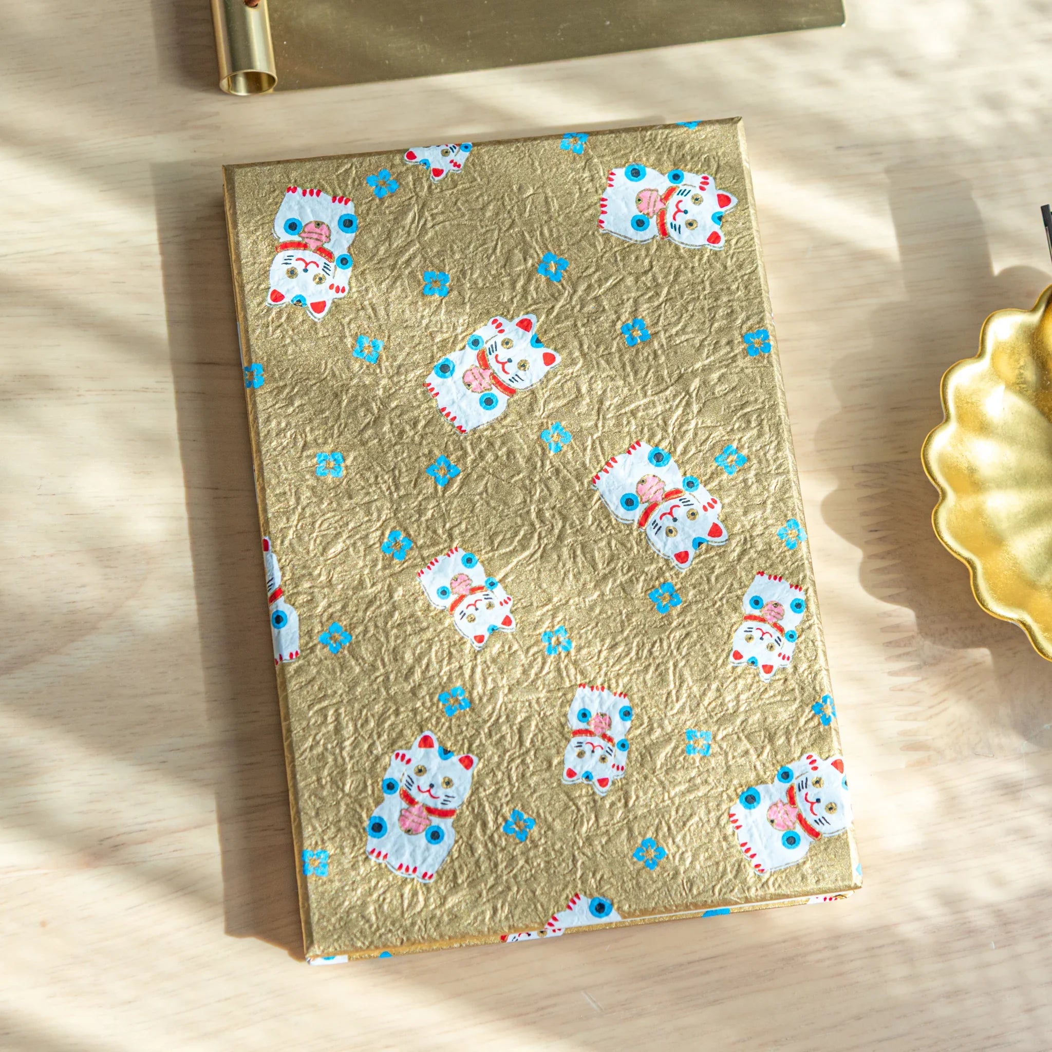 Gold washi Japanese goshuincho stamp book with maneki-neko lucky cat and blue flower pattern, overhead on wood surface