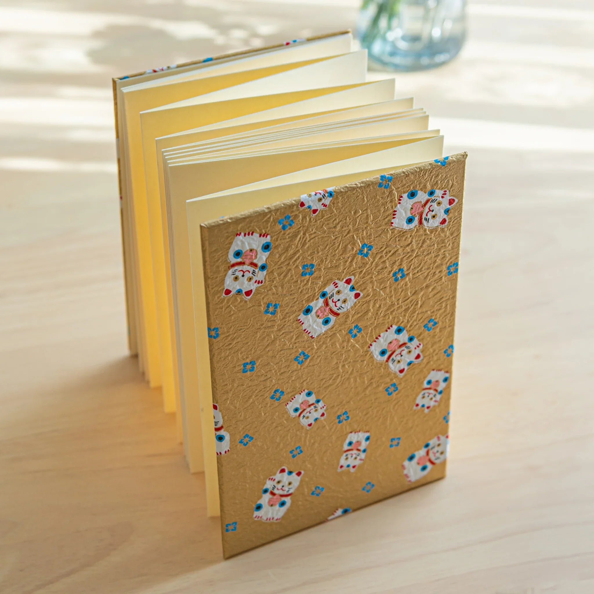 Gold maneki-neko washi Japanese goshuincho stamp book standing upright, accordion-fold cream pages fanning from the side
