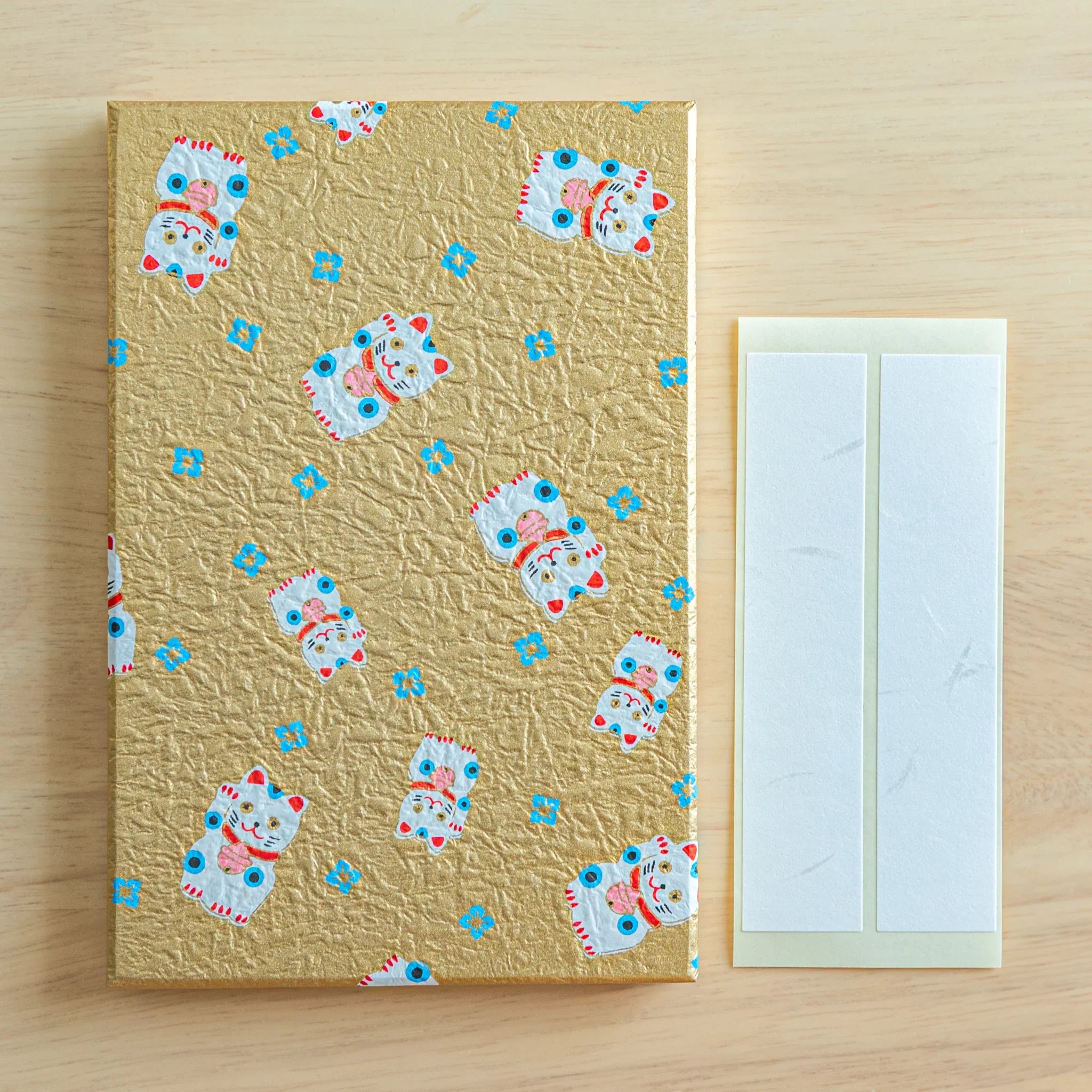 Gold maneki-neko washi Japanese goshuincho stamp book alongside two included white washi paper bookmark strips
