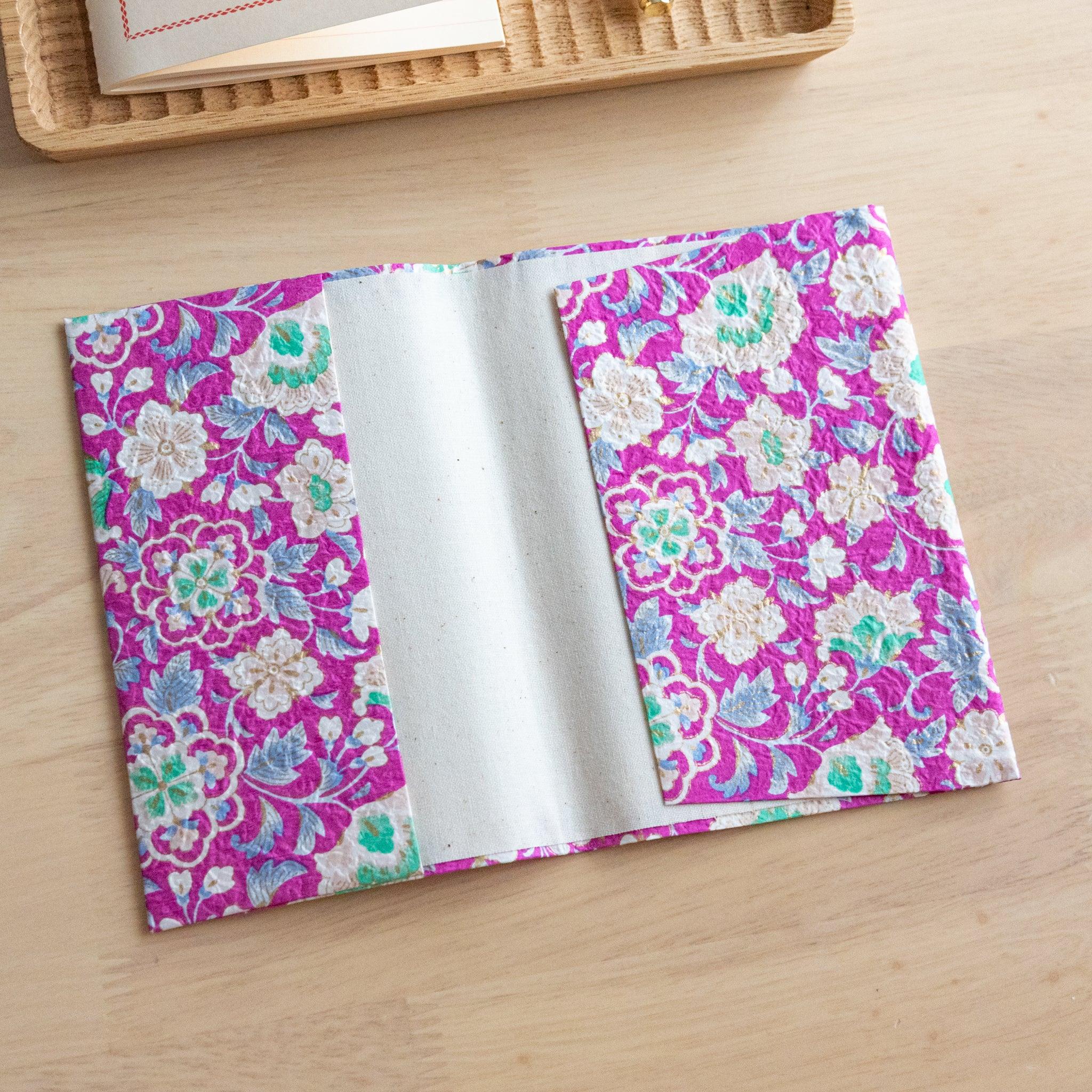 An open notebook cover with a vibrant pink floral pattern, revealing its inner white lining, placed on a wooden surface.