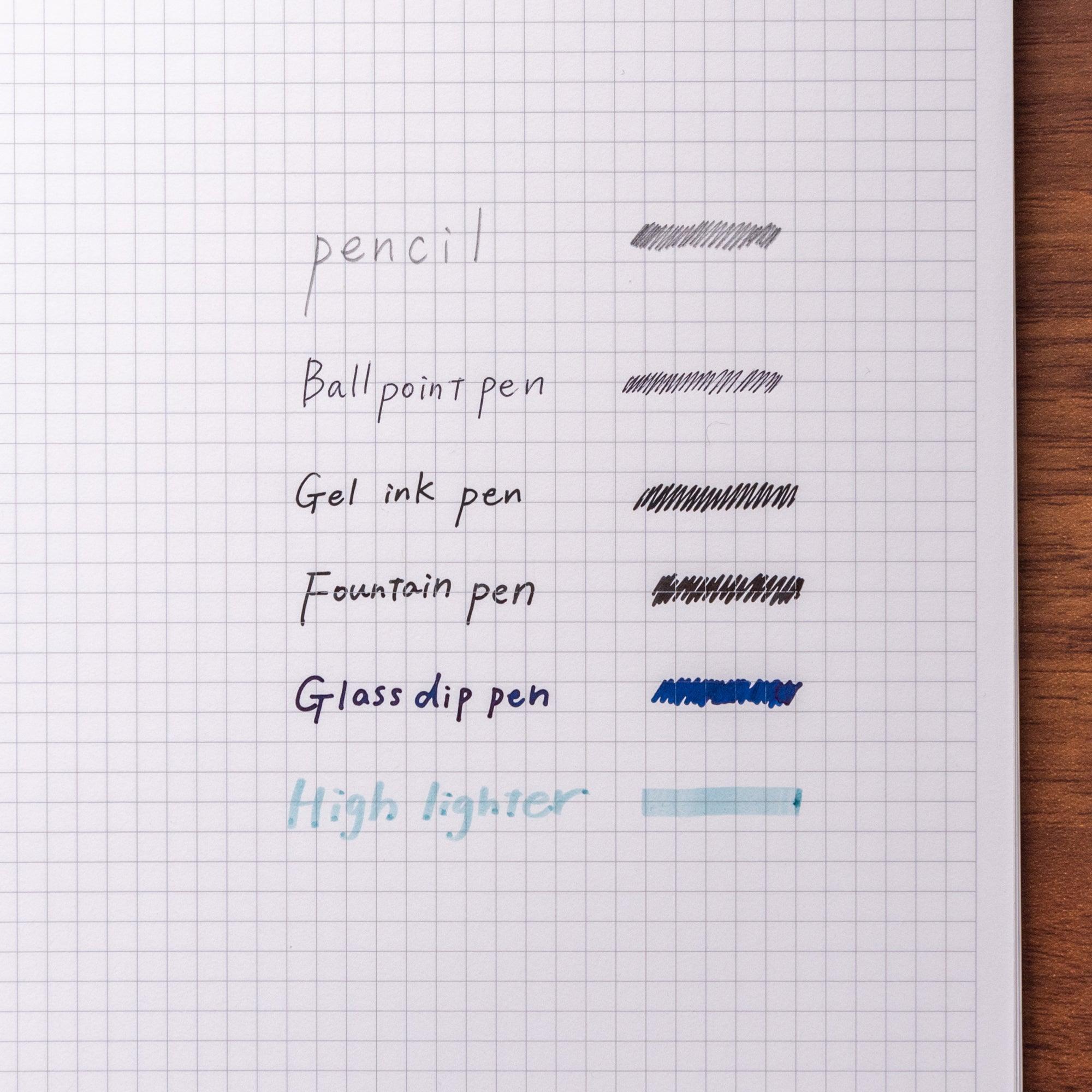 Japanese notebook featuring grid paper, with a page tested using various writing tools like pens and pencils, showcasing ink performance.