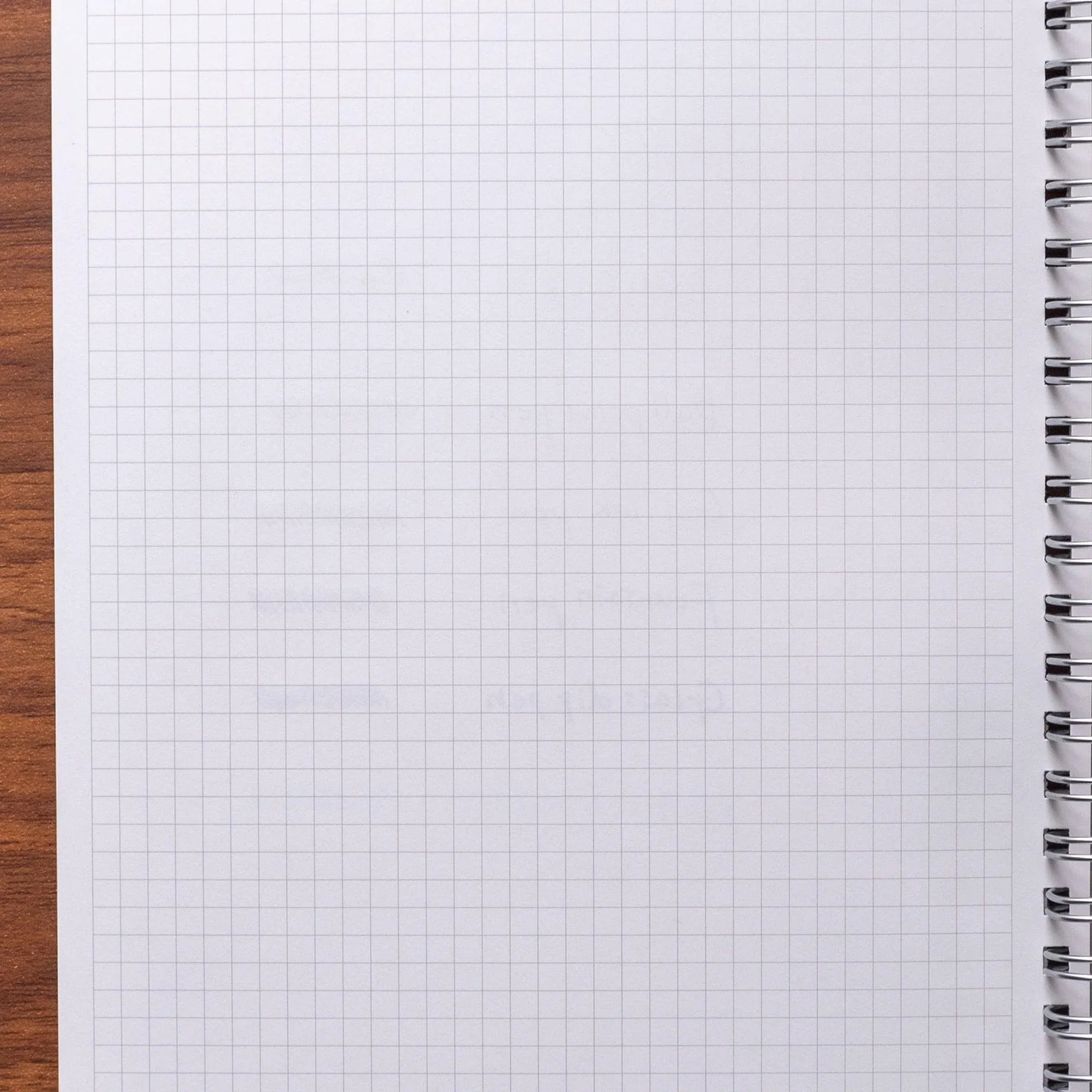 Blank fine grid page of Japanese yuzen washi notebook against wood surface, silver spiral binding visible at right edge