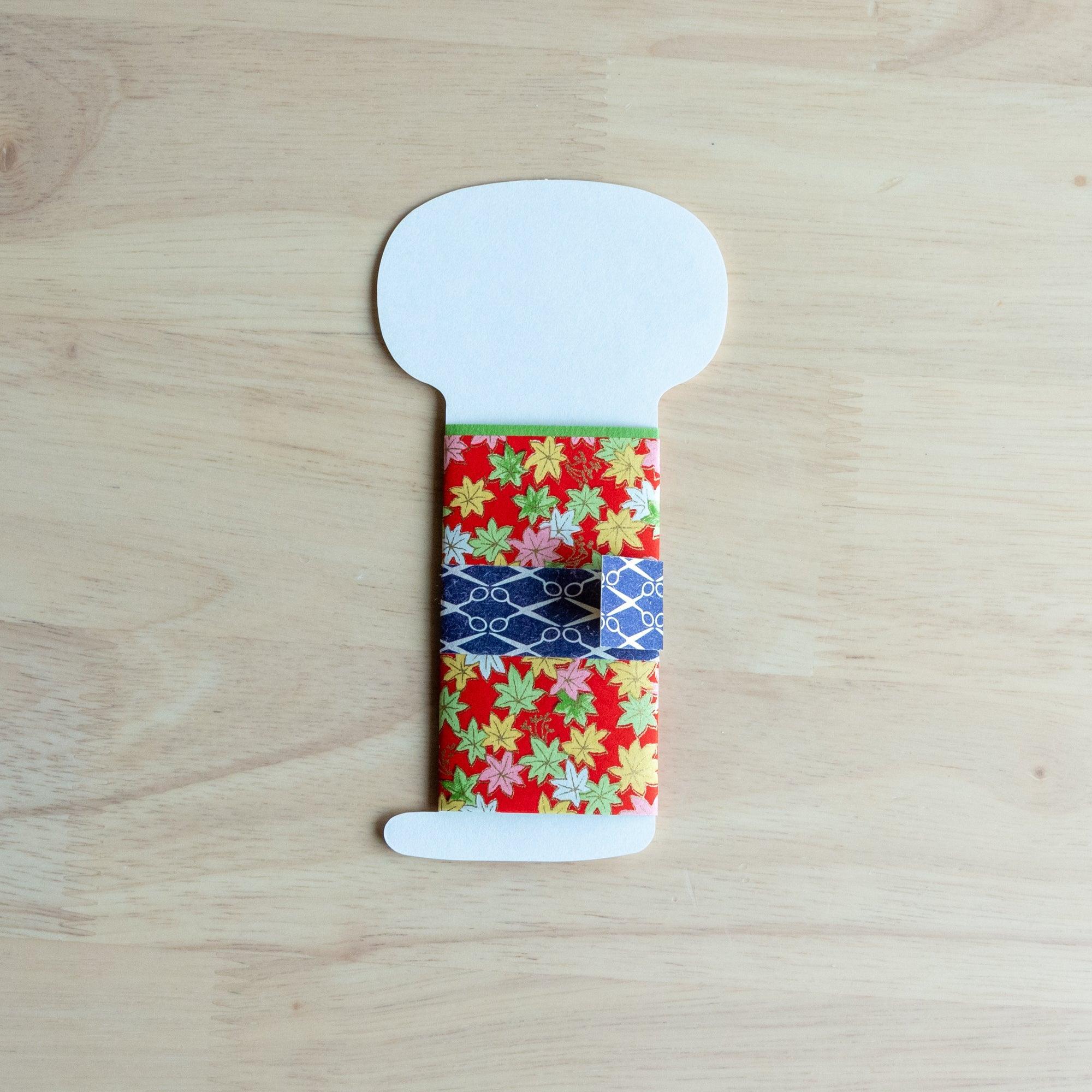 Reverse side of Maikohan Message Card showing blank white face area and closed red maple leaf yuzen washi kimono body on wood