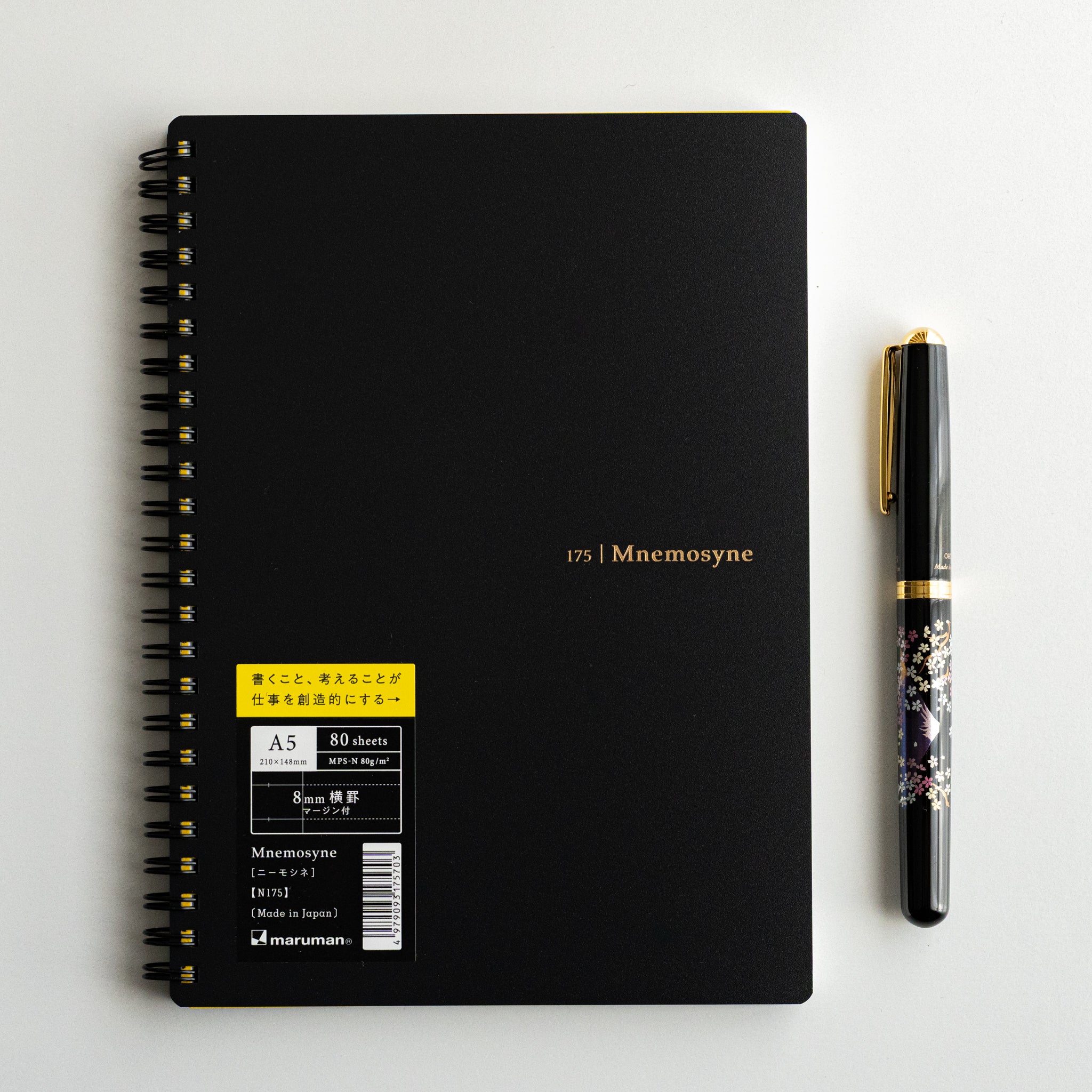 Black Maruman Mnemosyne notebook with spiral binding beside ornate pen, Japanese stationery for stylish notes