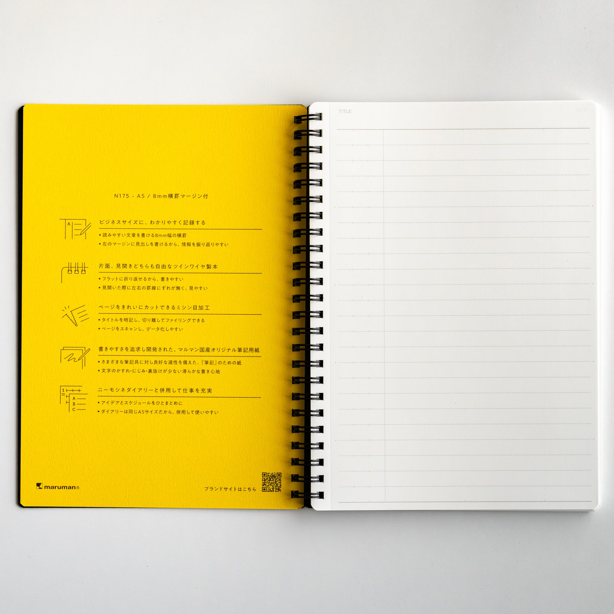 Maruman Mnemosyne lined notebook opened to reveal a yellow inside cover with Japanese instructions and a ruled white page, spiral bound.