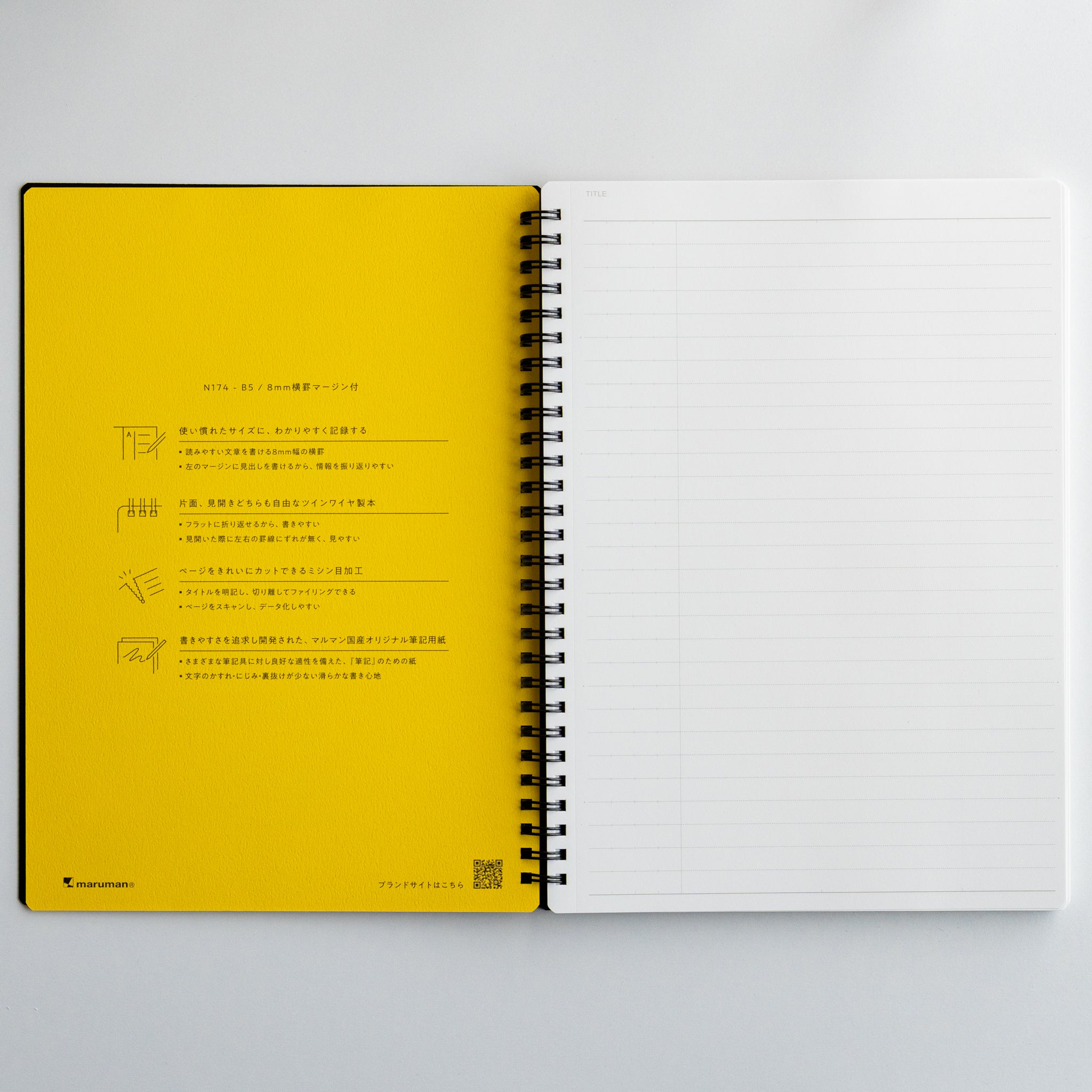 Open Maruman Mnemosyne notebook with yellow printed page beside blank lined page, featuring twin-ring binding.
