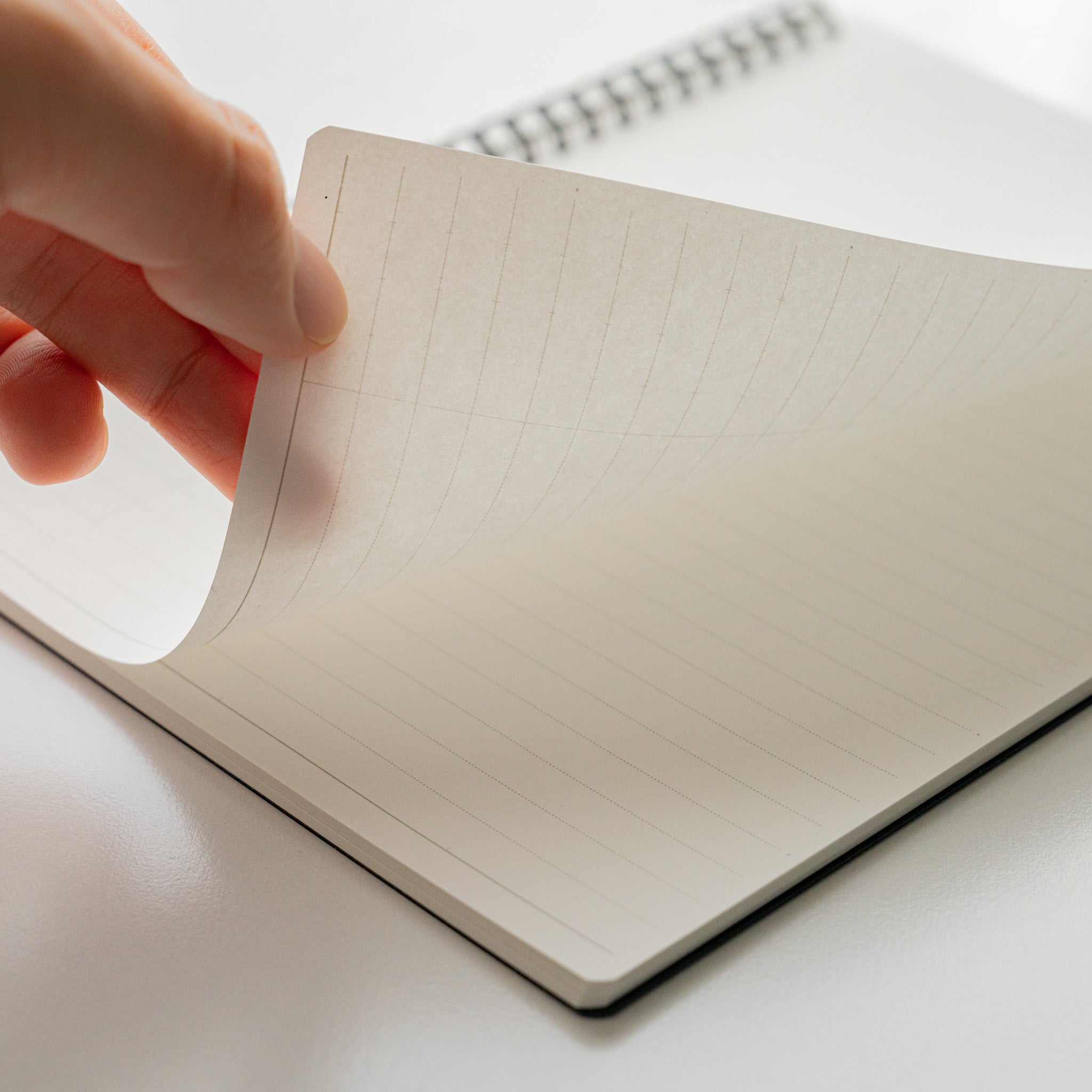 Hand turning a page of the Maruman Mnemosyne lined notebook, revealing smooth pages and twin-ring binding.