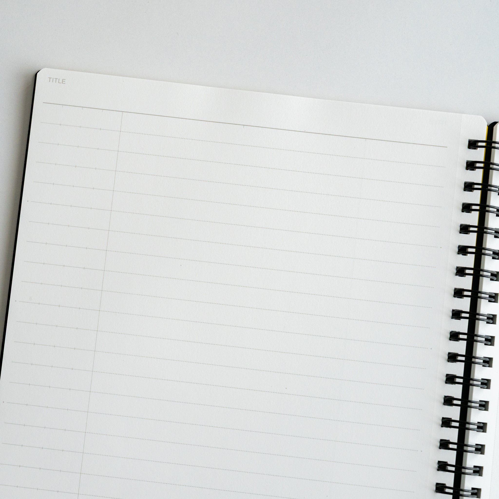 Open Maruman Mnemosyne notebook at an angle, displaying blank 8 mm lined pages with black spiral binding.