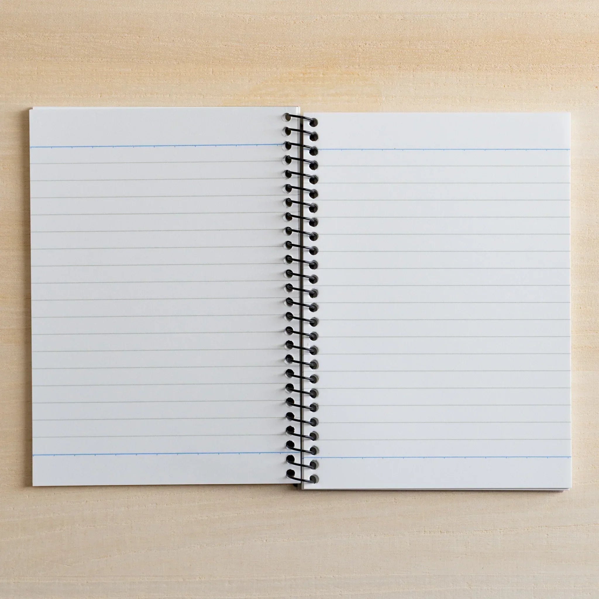 Japanese notebook by maruman with spiral binding, open on a light wood desk showing lined white pages with blue lines.