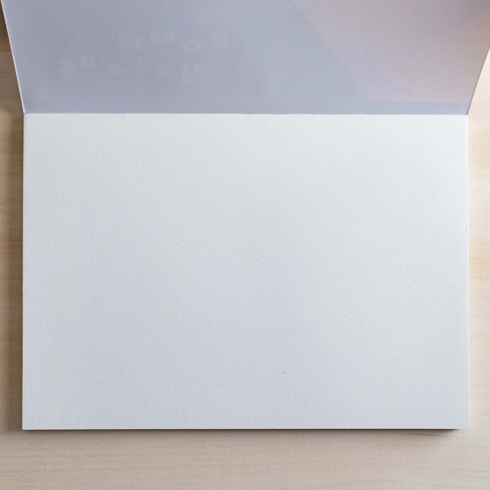 Open Maruman Japanese sketchbook with a translucent protective sheet and a blank white textured page, ideal for arts and crafts.