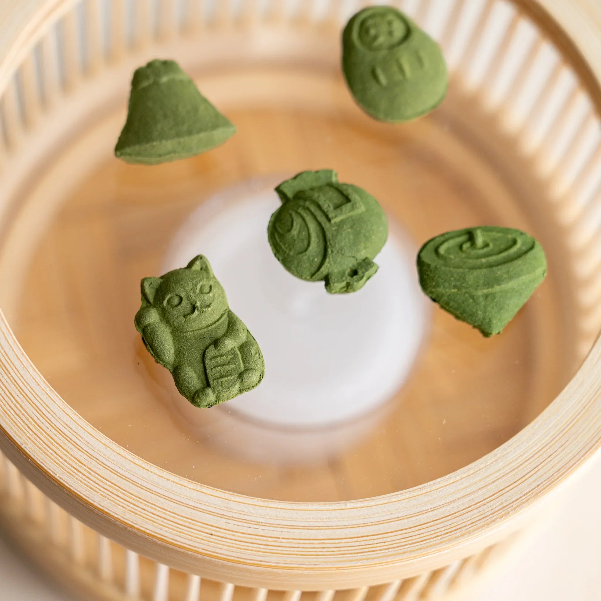 Five pressed matcha incense pieces in lucky-charm shapes on the heat-resistant glass plate of the Suruga bamboo warmer