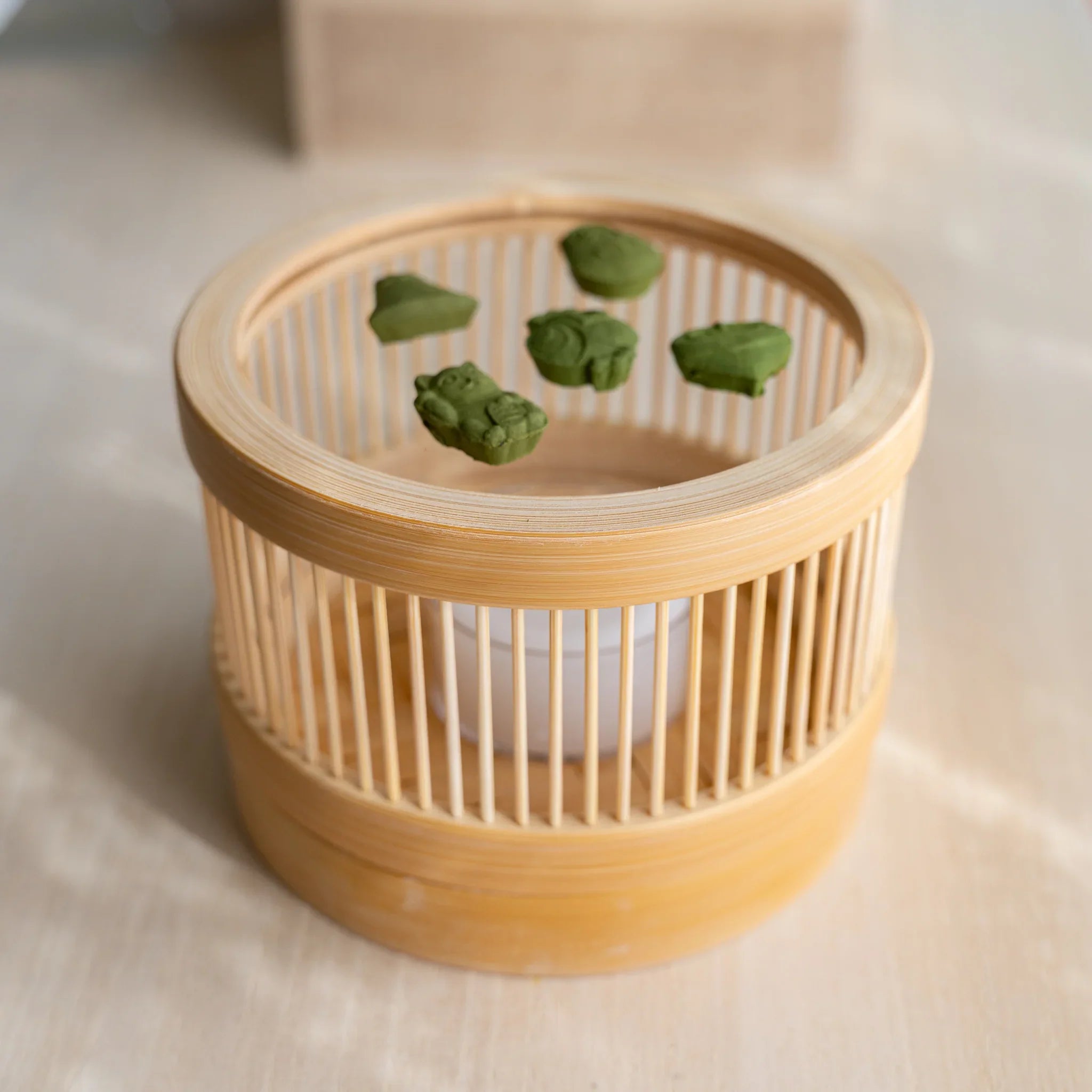 Top-down close-up of pressed matcha incense pieces in lucky-charm shapes inside the Suruga bamboo warmer