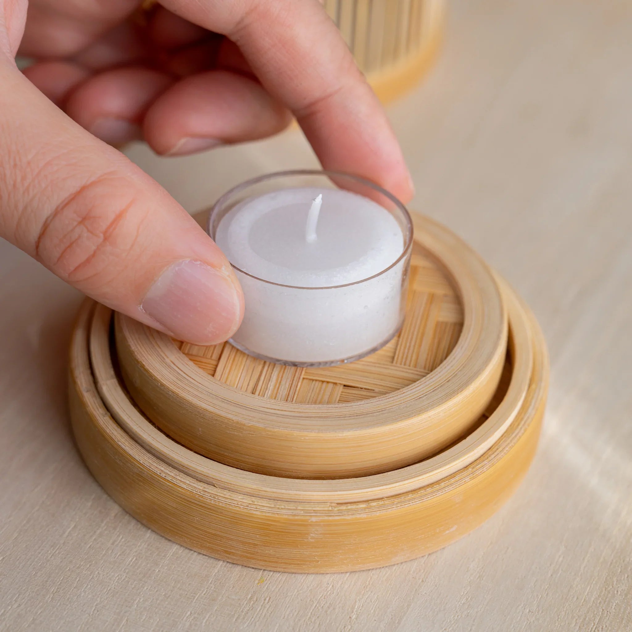 Hand placing tealight on the woven bamboo base of the Suruga matcha incense warmer with the lid set on top