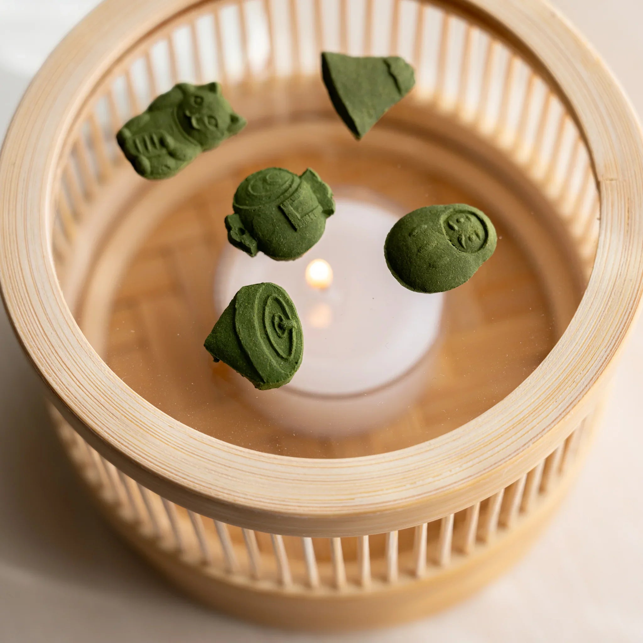 Hand lifting the woven bamboo lid of the Suruga matcha incense tea warmer to reveal the tealight inside