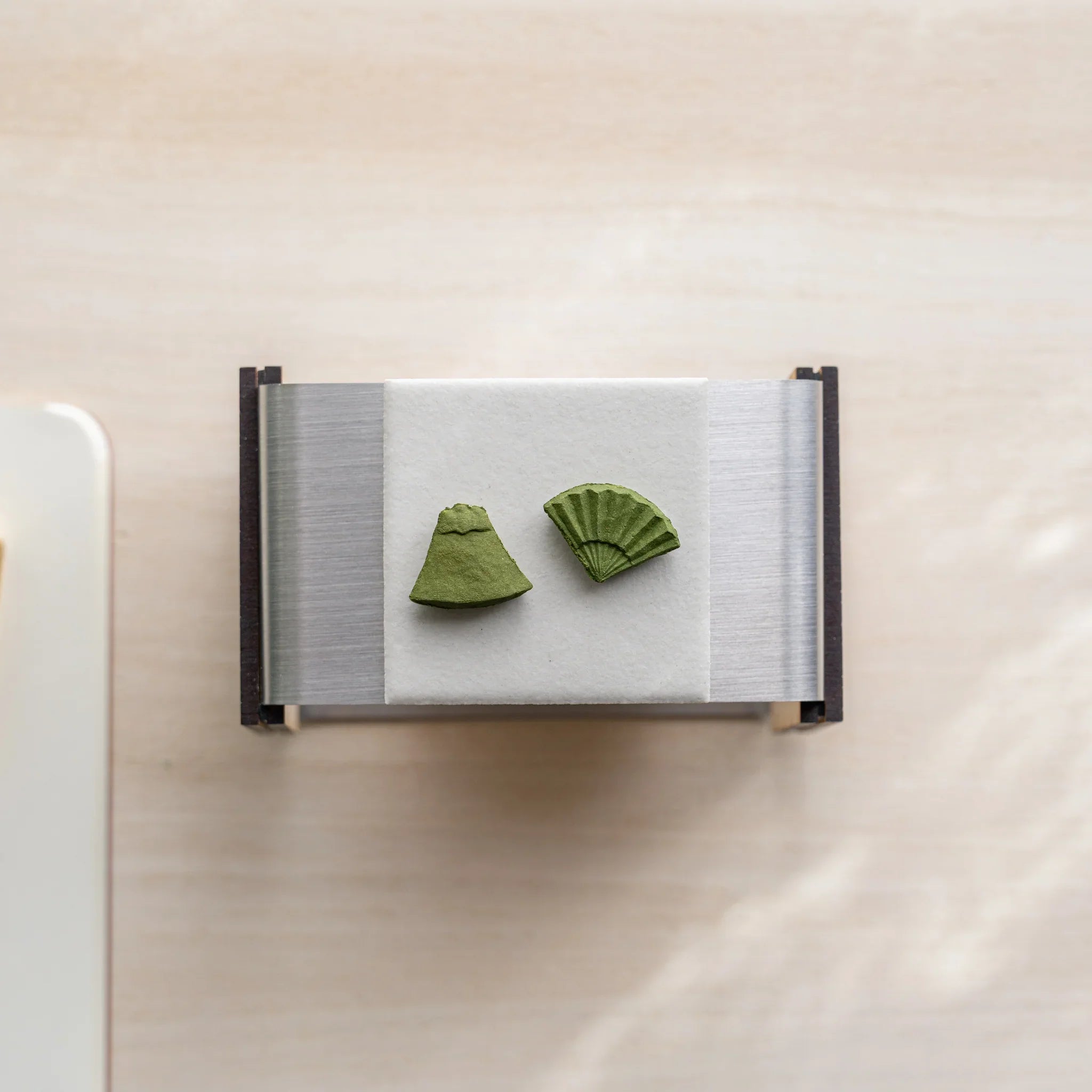 Top-down view of foldable matcha incense tea warmer with two pressed matcha incense pieces on the ceramic plate