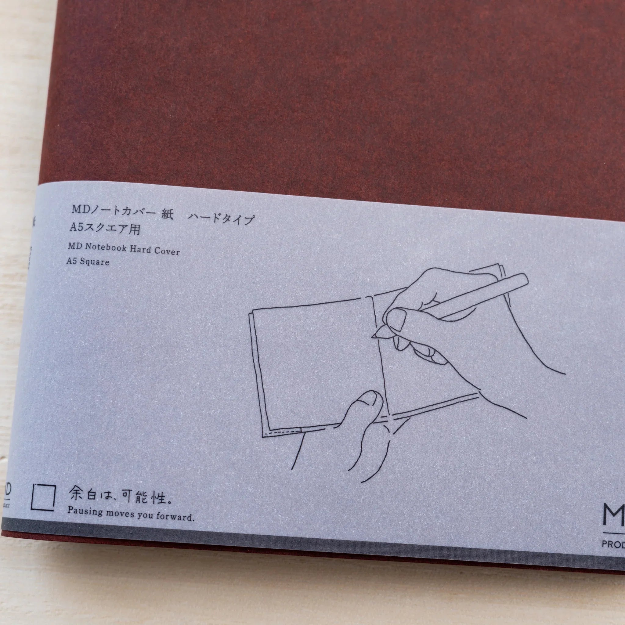 Grey belly band of MD Notebook Hard Cover A5 Square with a hand-with-pen line drawing and MD PRODUCT logo