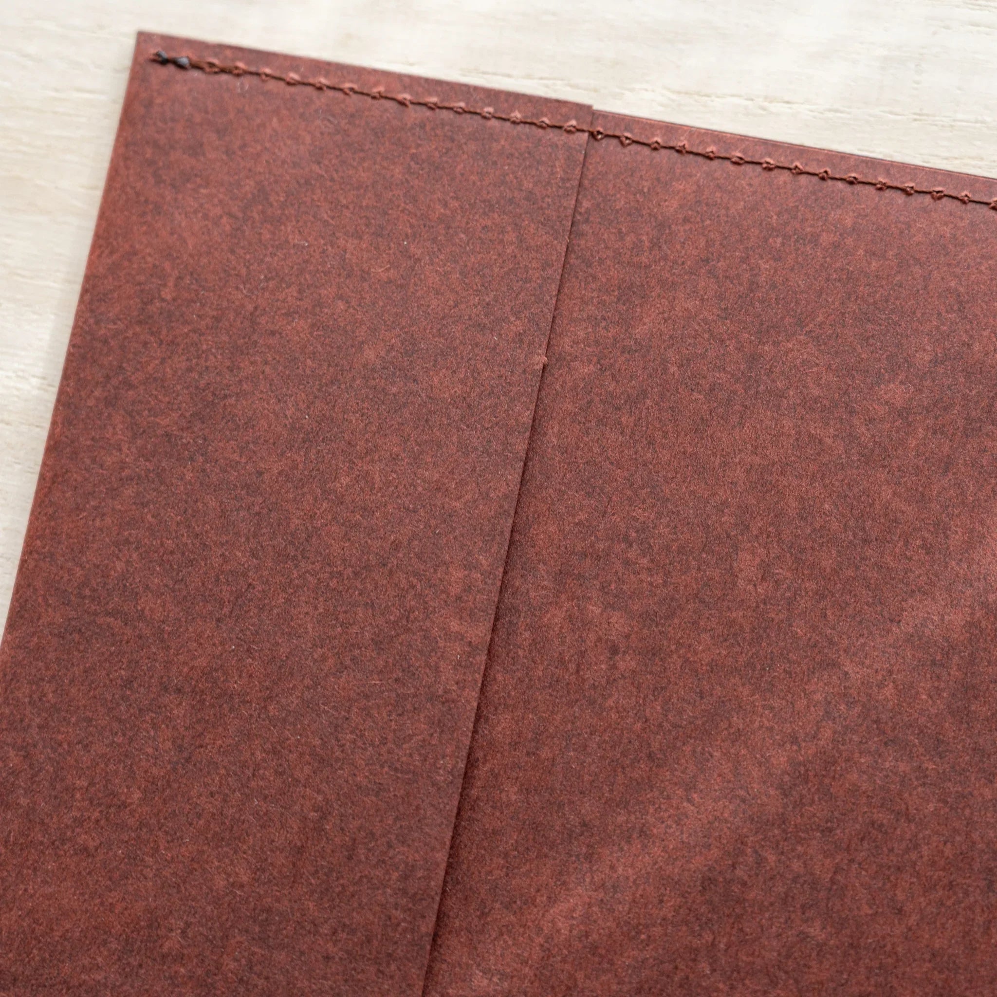 Midori MD Notebook Hard Cover corner close-up showing dark red hard paper texture, stitched top edge, and center fold line