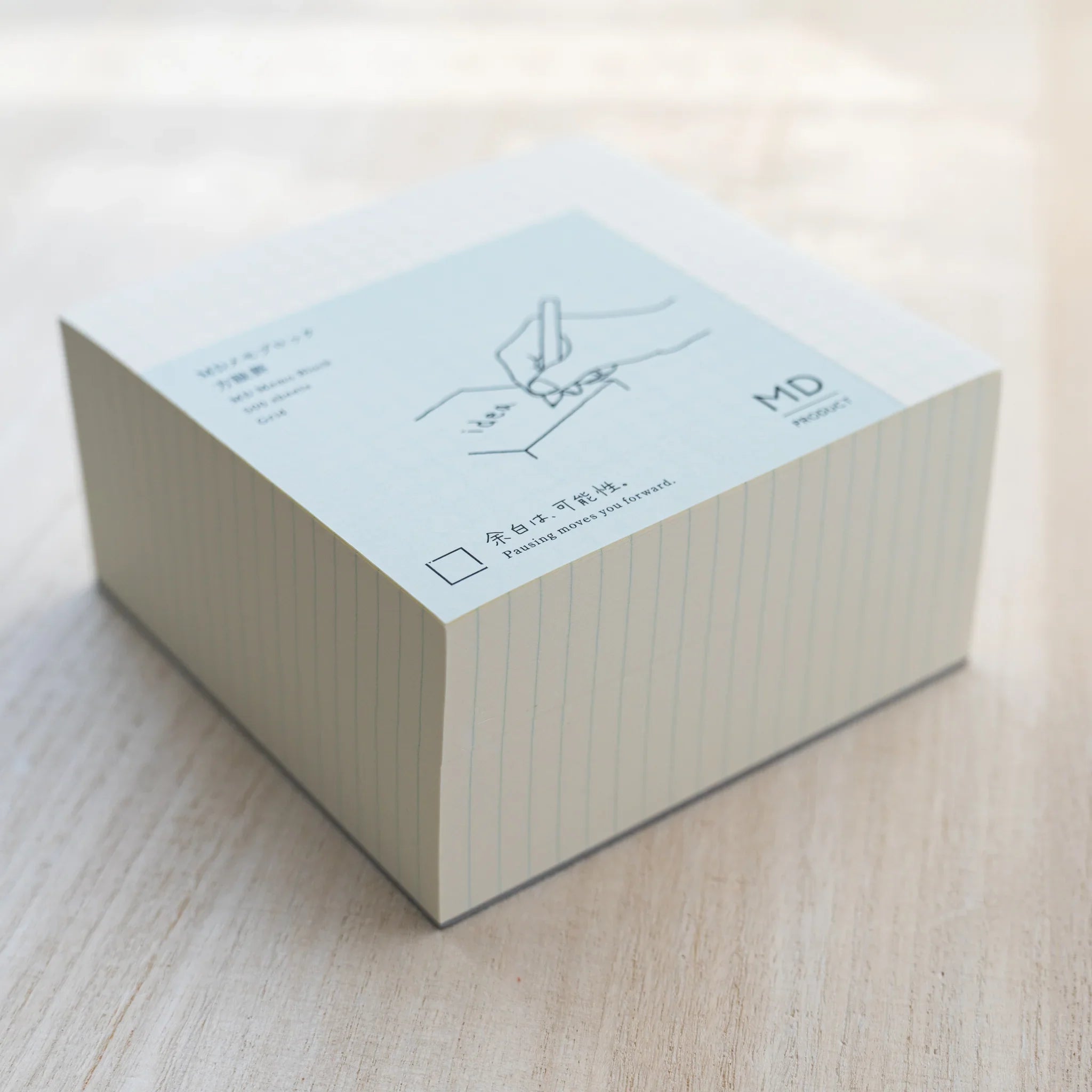 Angled MD Memo Block grid type, cream paper with light blue wrap showing hand illustration and MD Product logo