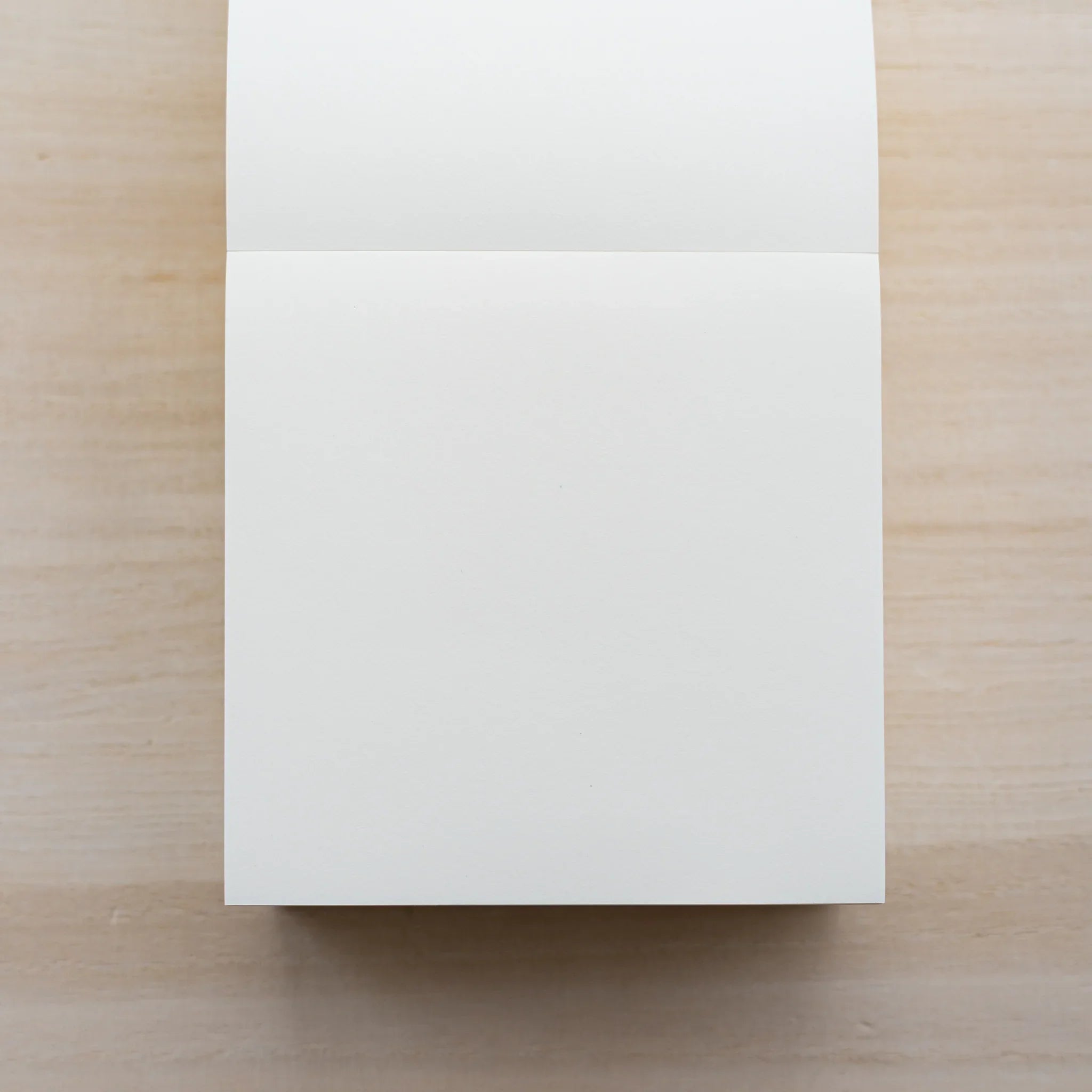 MD Memo Block opened to a blank white sheet with the top sheet folded back, on a wood surface