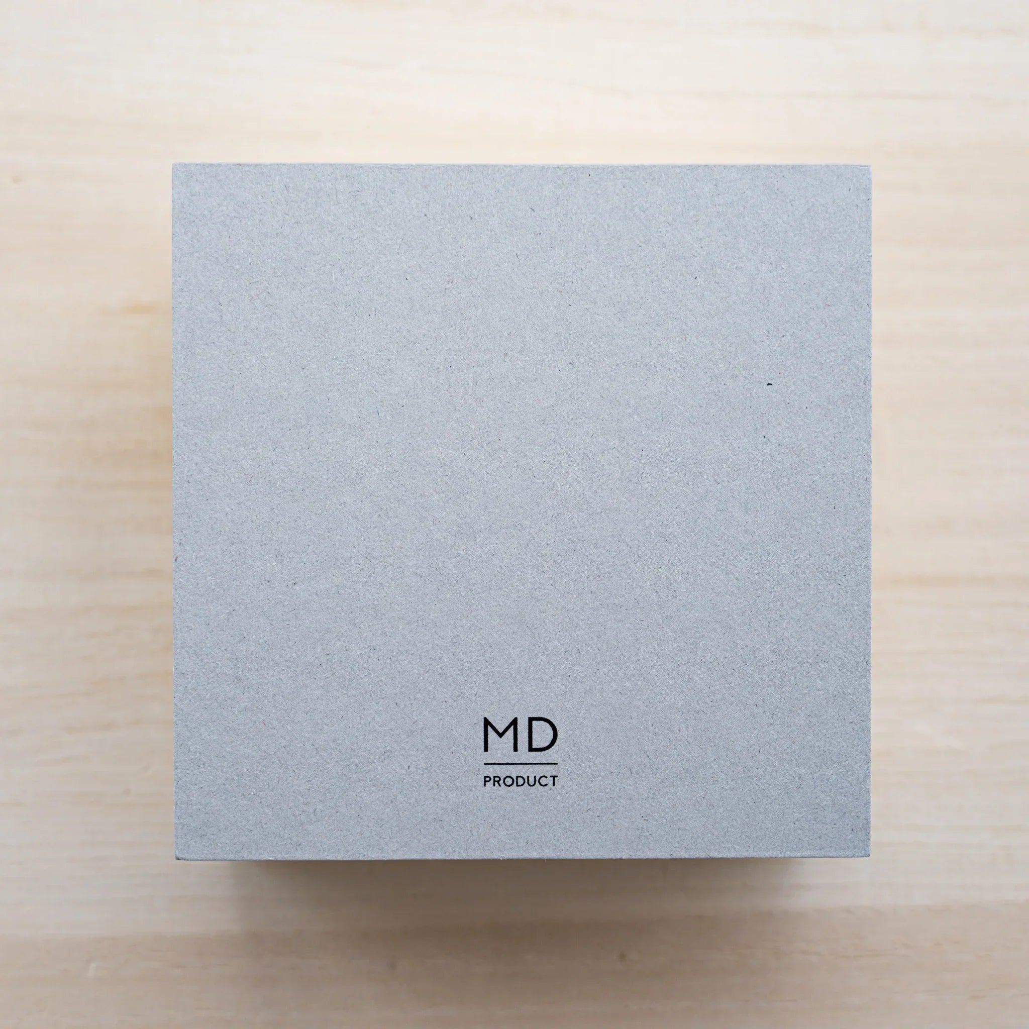 Gray cardboard backing of an MD Memo Block with black MD Product logo, top view on wood