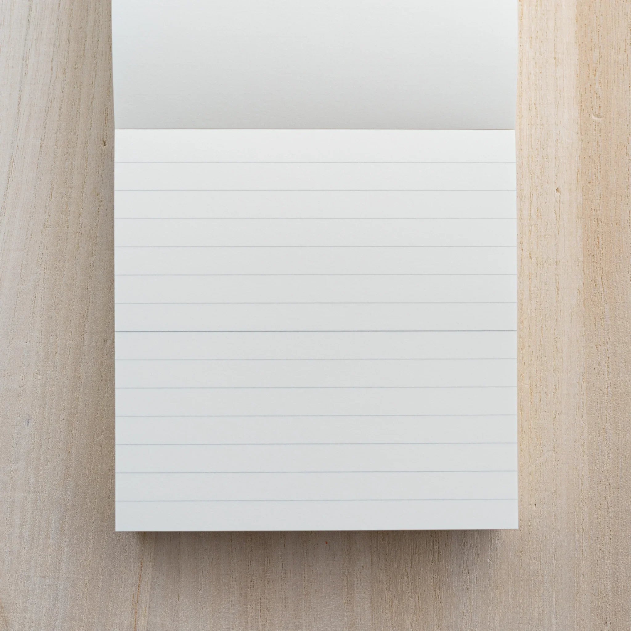 MD Memo Block opened to a sheet with faint horizontal ruled lines, on a wood surface