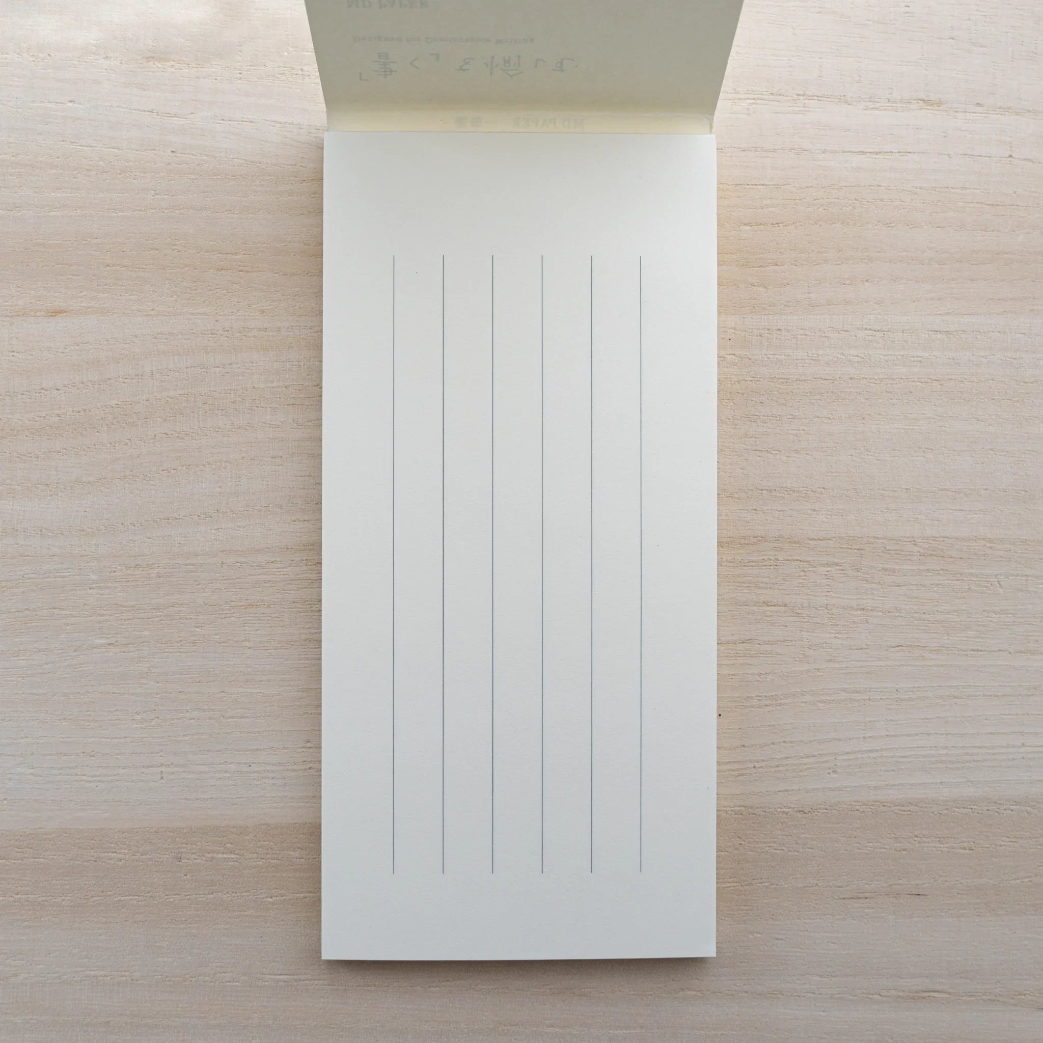 MD Paper letter pad opened to a white sheet with vertical ruled lines on a wood surface