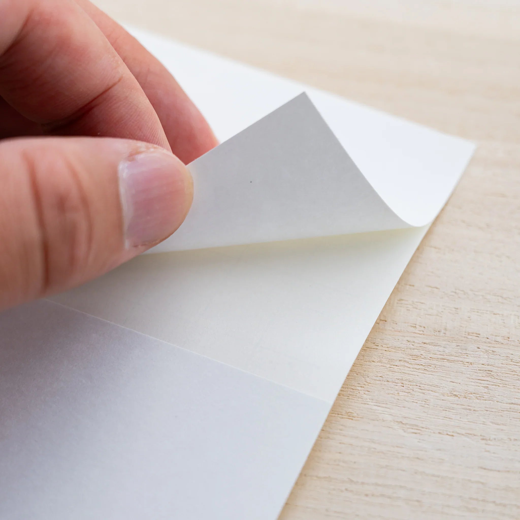 Hand peeling a blank white MD Diary Sticker sheet from its backing on a wood surface