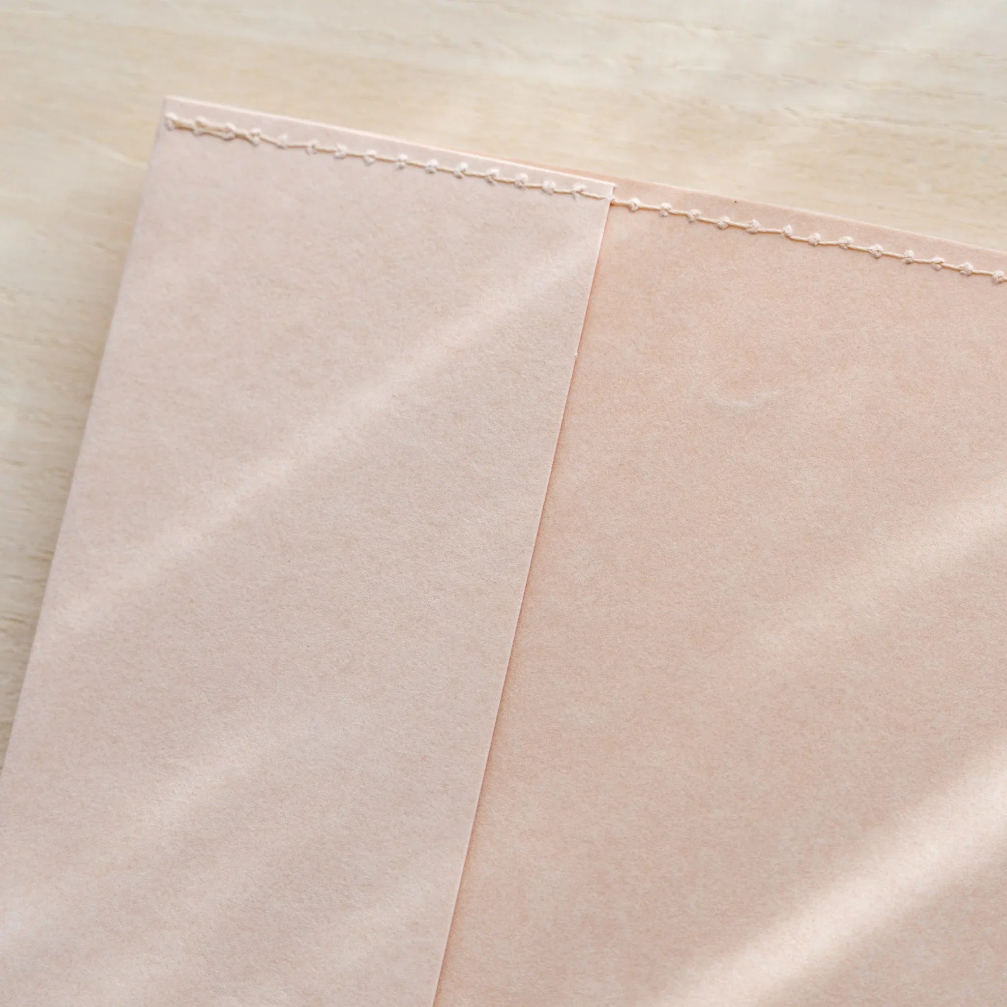 Midori MD Notebook Paper Cover angled close-up showing pale paper panels and stitched top edge detail on wood surface