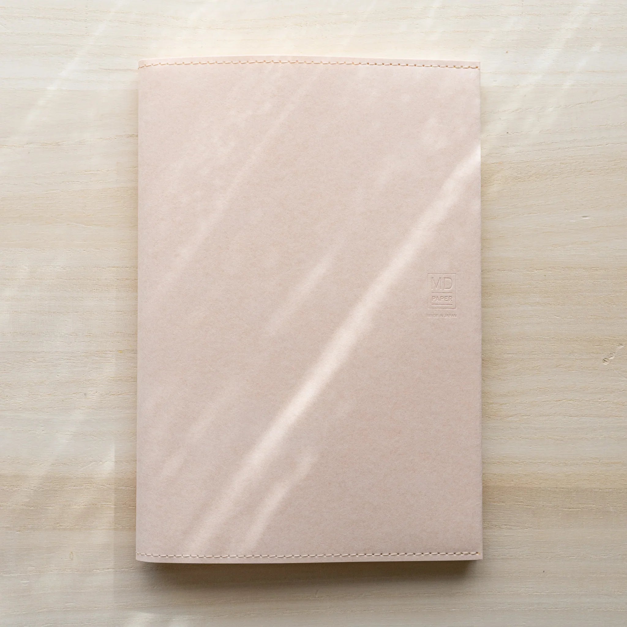 Midori MD Notebook Paper Cover closed with notebook inside, pale pink paper showing embossed MD Paper logo and stitched edges