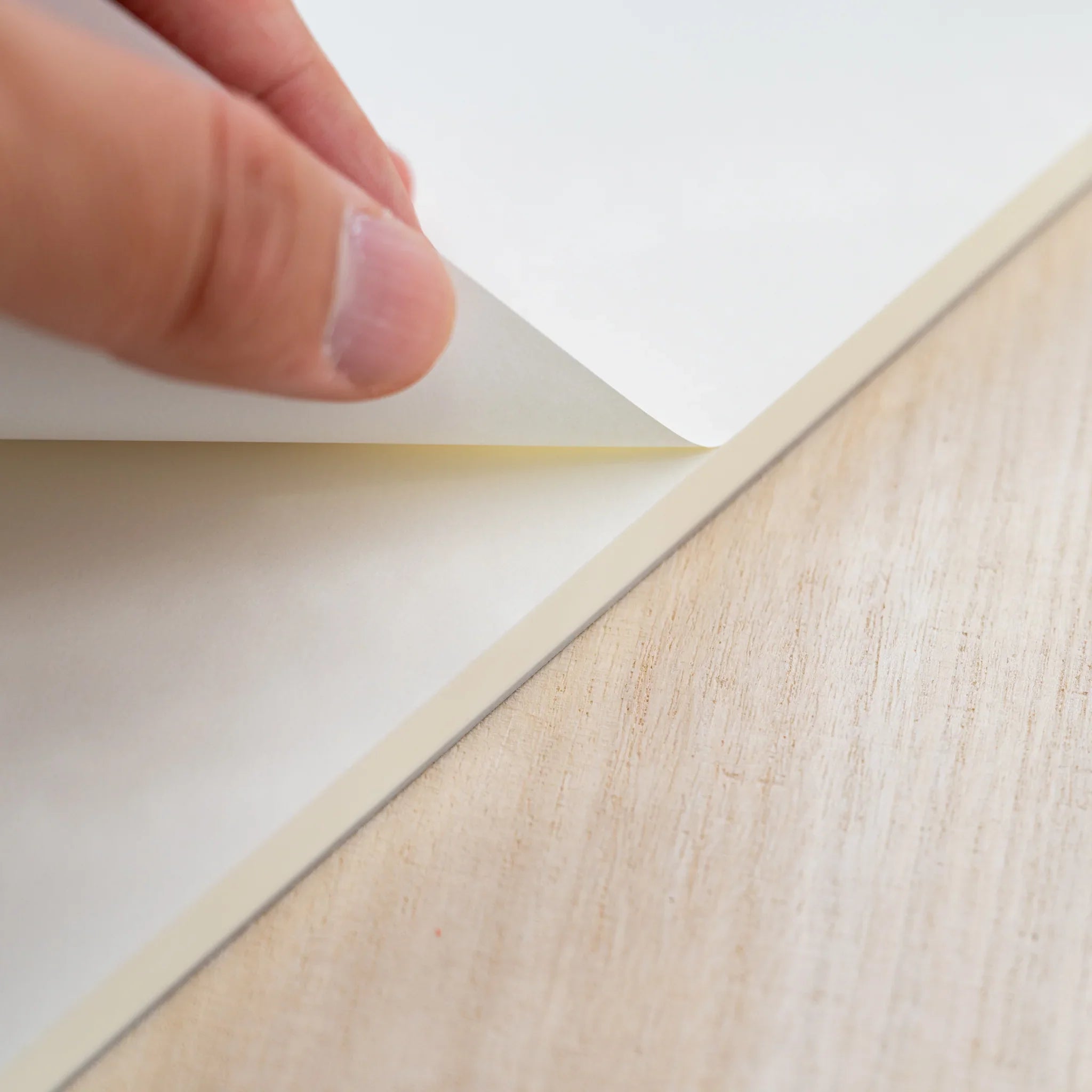A hand peeling a blank cream sheet from the glued top edge of a Midori MD Paper Pad A4
