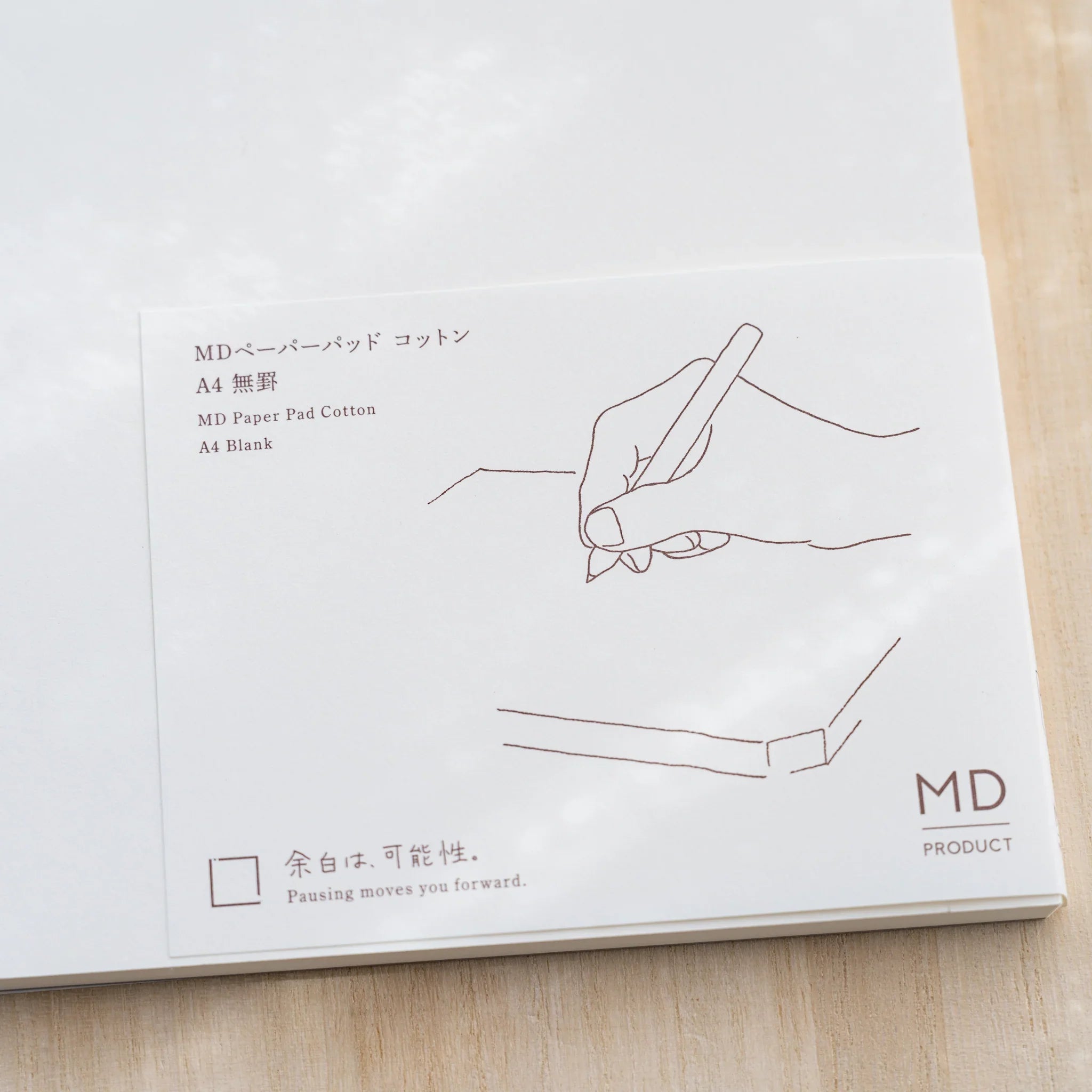 Close-up of Midori MD Paper Pad Cotton A4 belly band in brown, hand-writing line drawing and MD Product logo